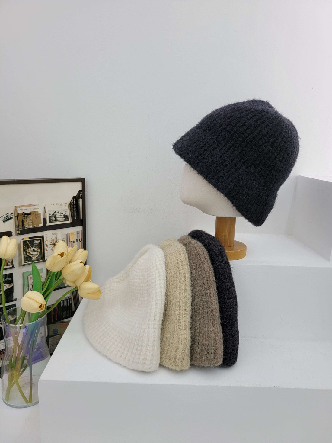 Black, brown, and beige beanies on a mannequin head against a white wall.