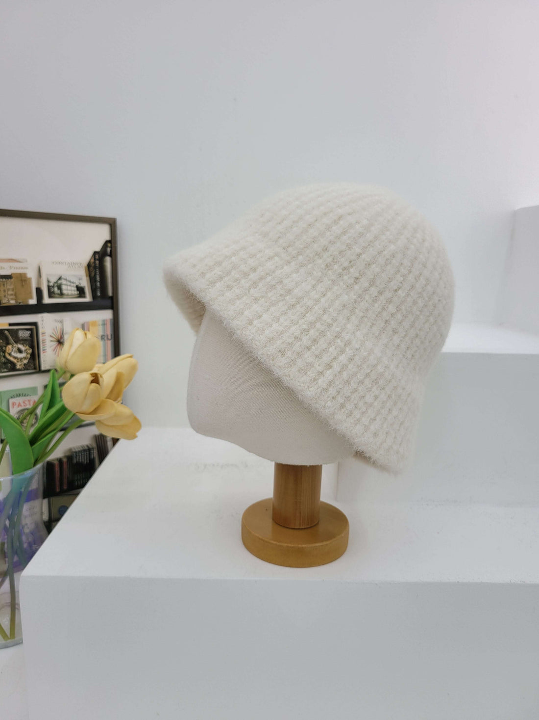 White textured wall hook with wooden handle on a white wall, with a small plant below.