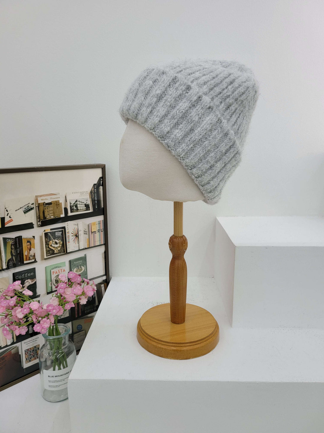 Gray knit beanie on a mannequin head with a wooden lamp against a white wall.