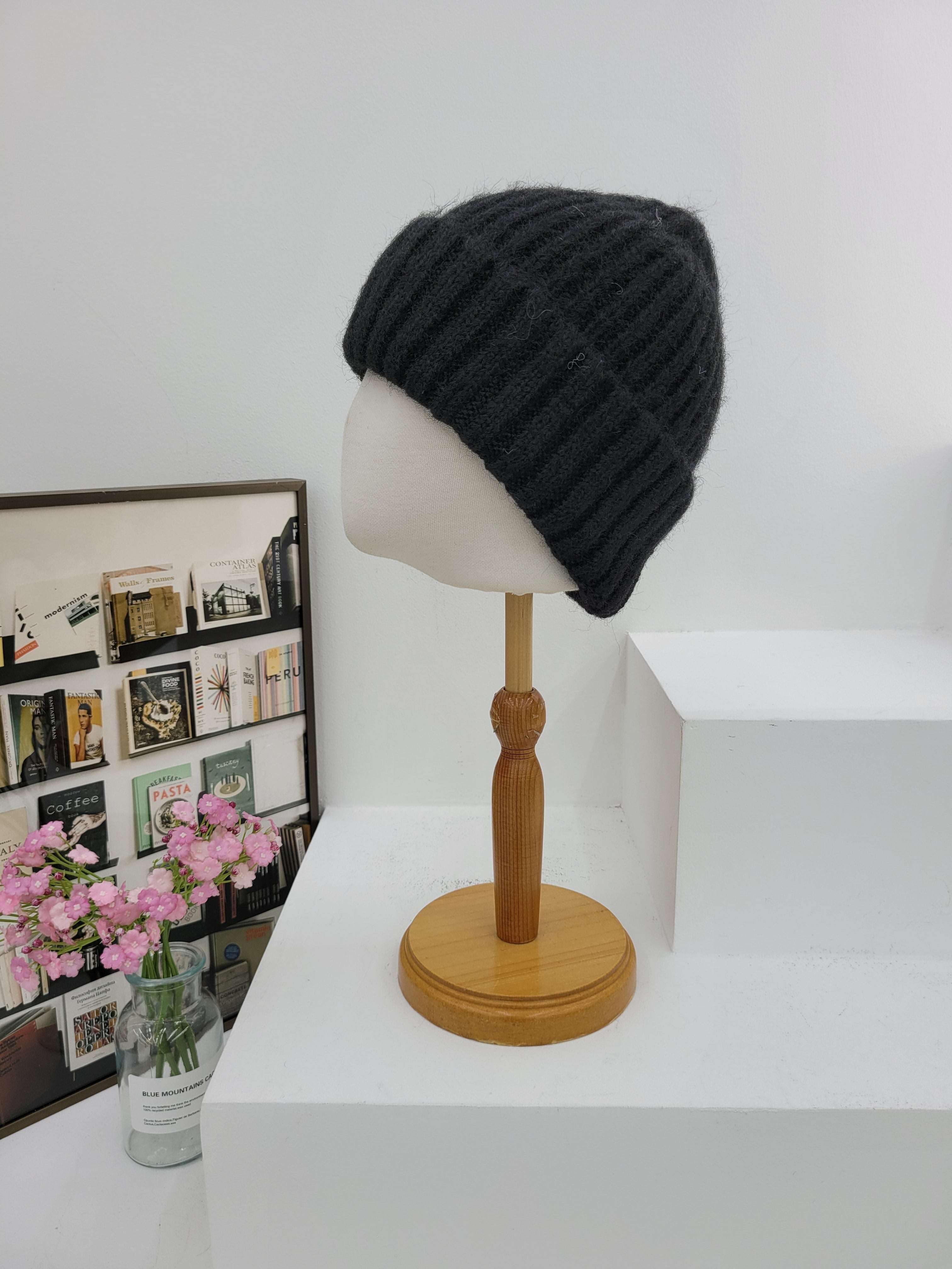 Black knit beanie on a mannequin head against a white wall with a wooden lamp.