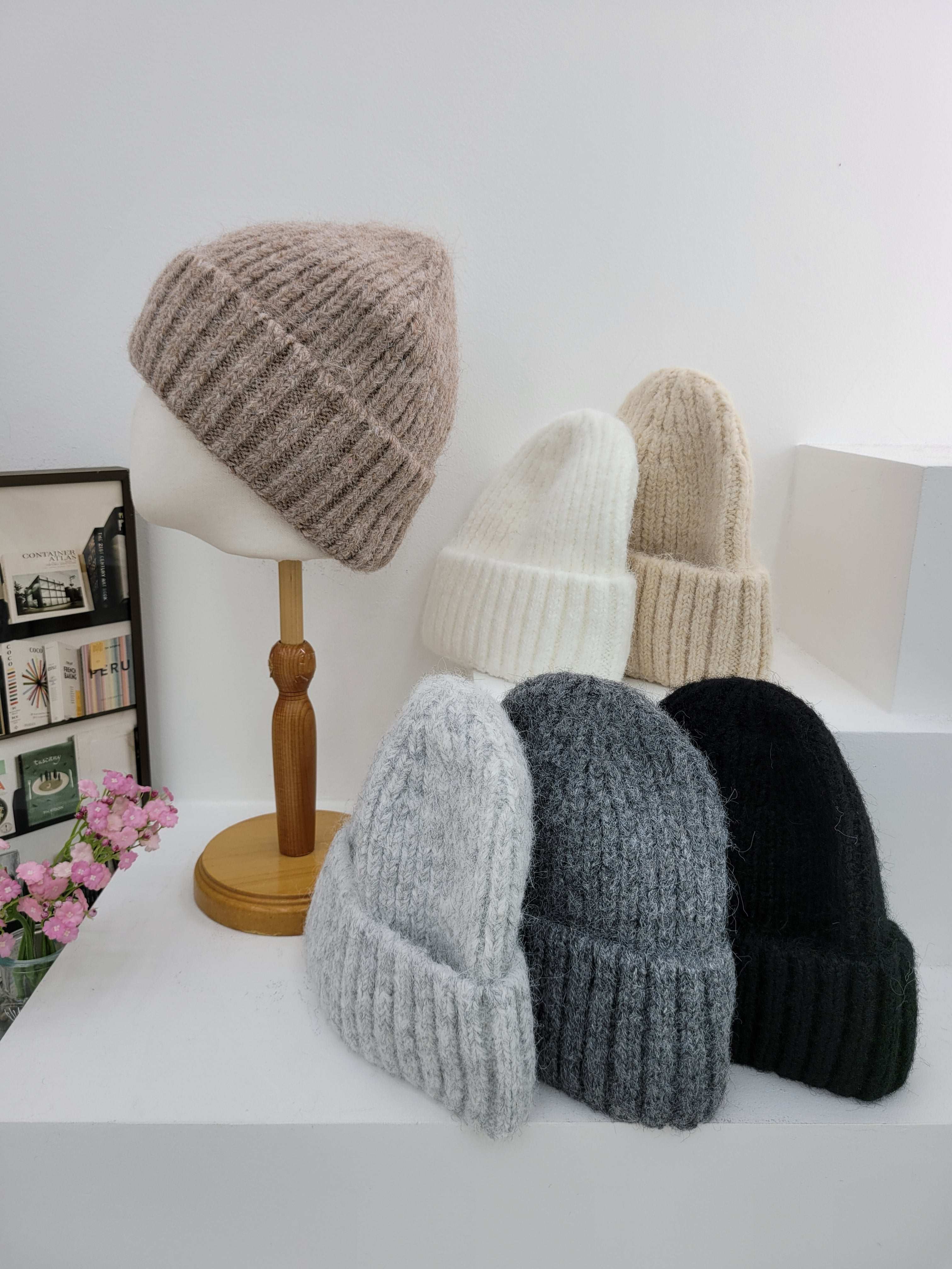 Set of knitted hats in various colors on a white surface with a lamp and decorative items in the background.