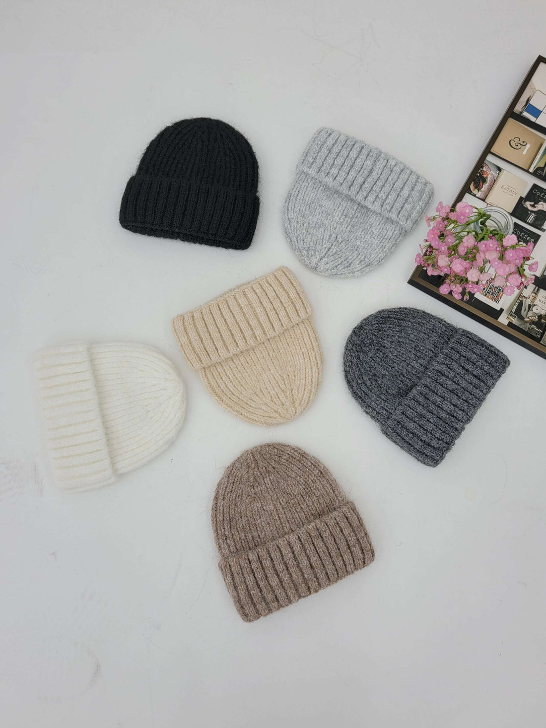 Set of six knit beanie hats in various colors on a light surface.