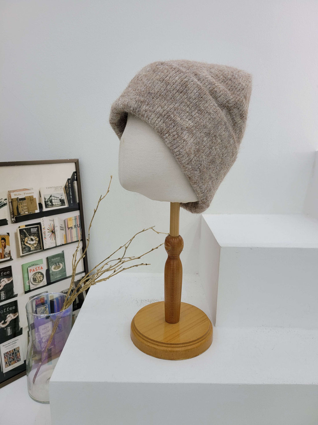 Brown knitted beanie on a mannequin head against a white wall with a decorative frame below.