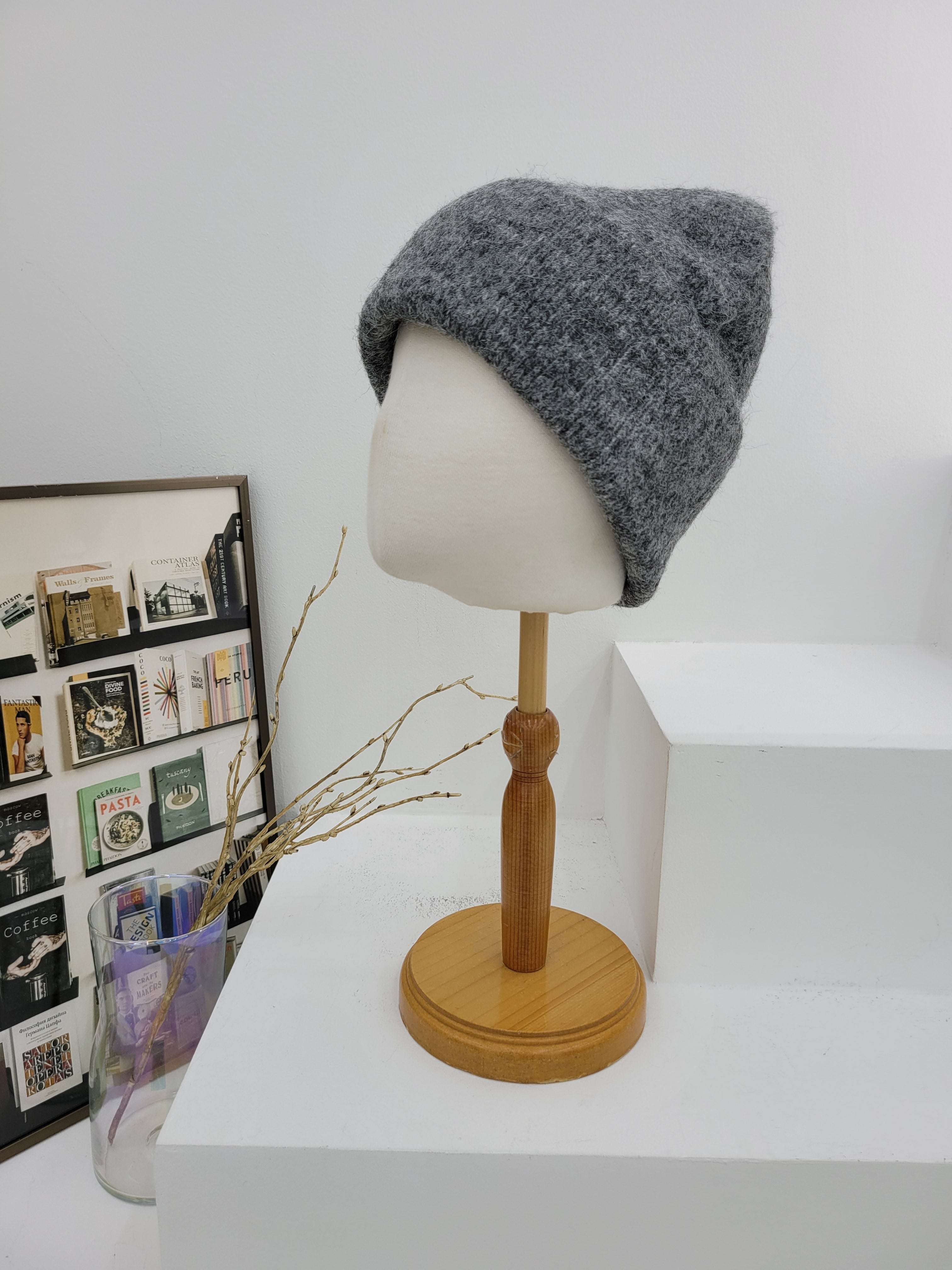 Gray knit beanie on a mannequin head with a wooden lamp against a white wall.