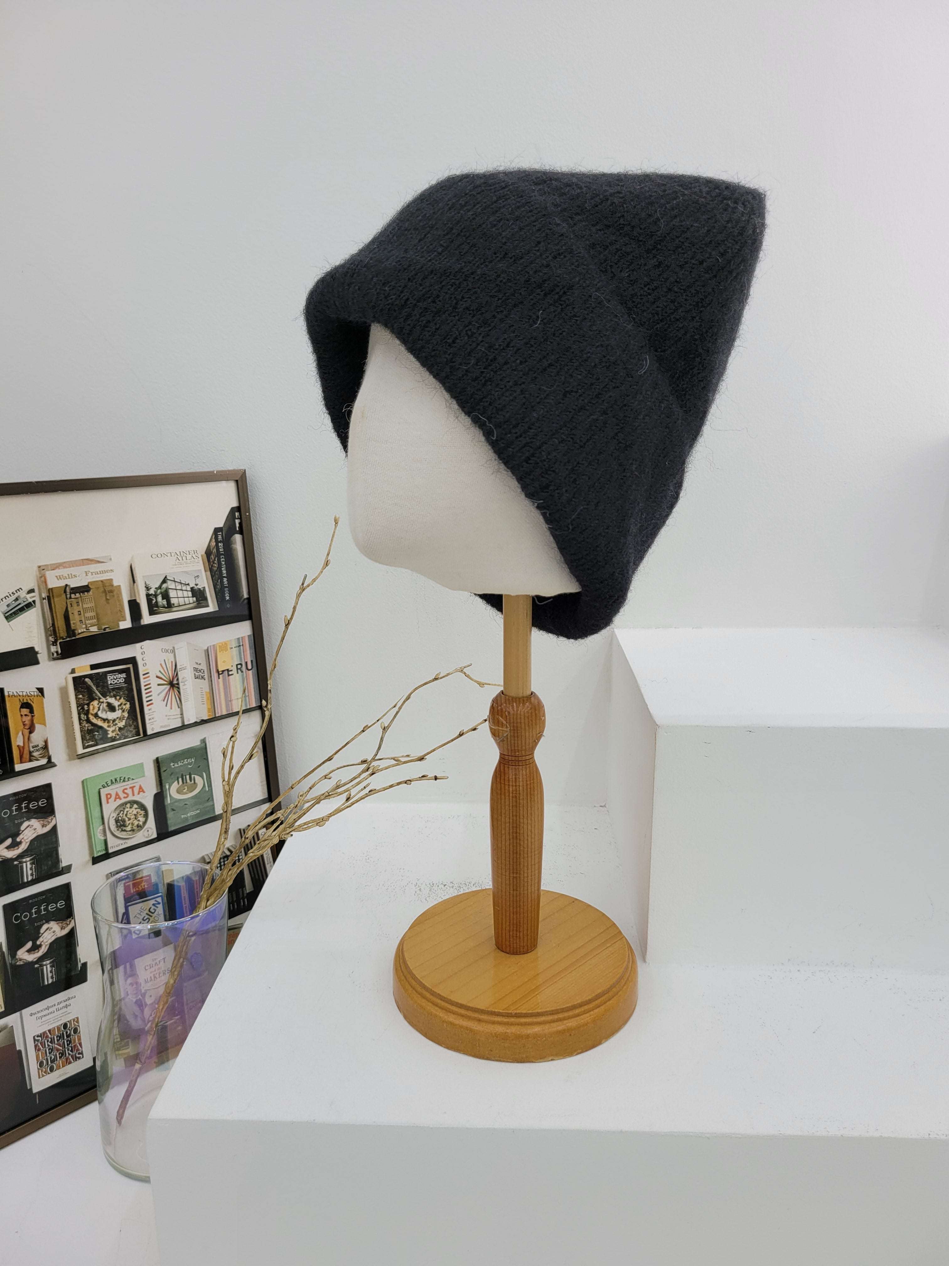 Black beanie on a mannequin head with a wooden lamp against a white wall.