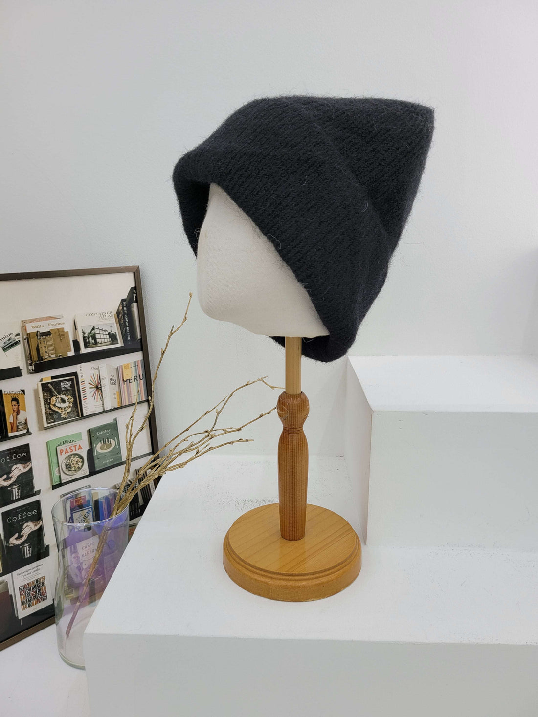 Black beanie on a mannequin head with a wooden lamp against a white wall.