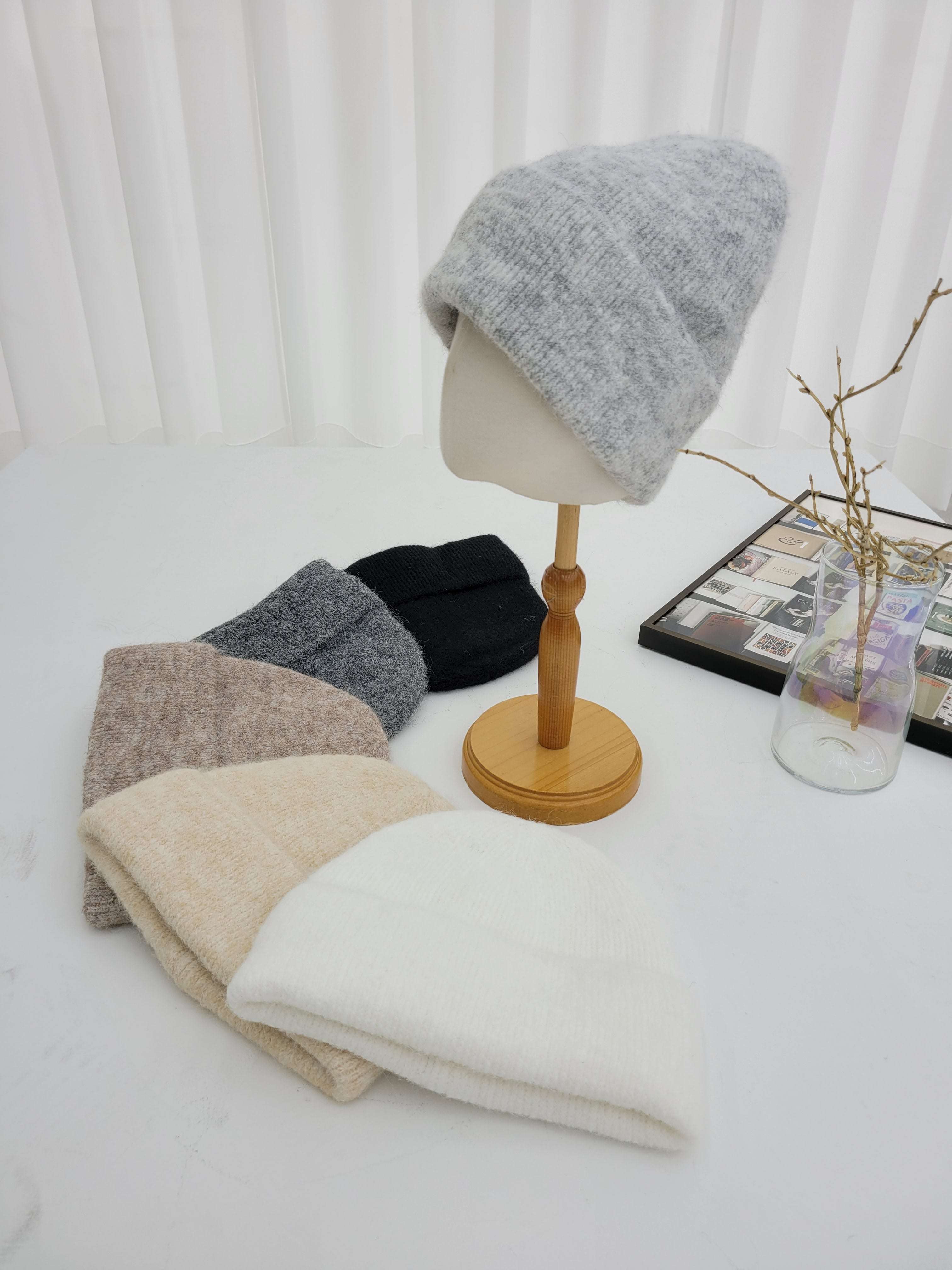 Mannequin head with gray knit cap on a white surface with other caps in the background.