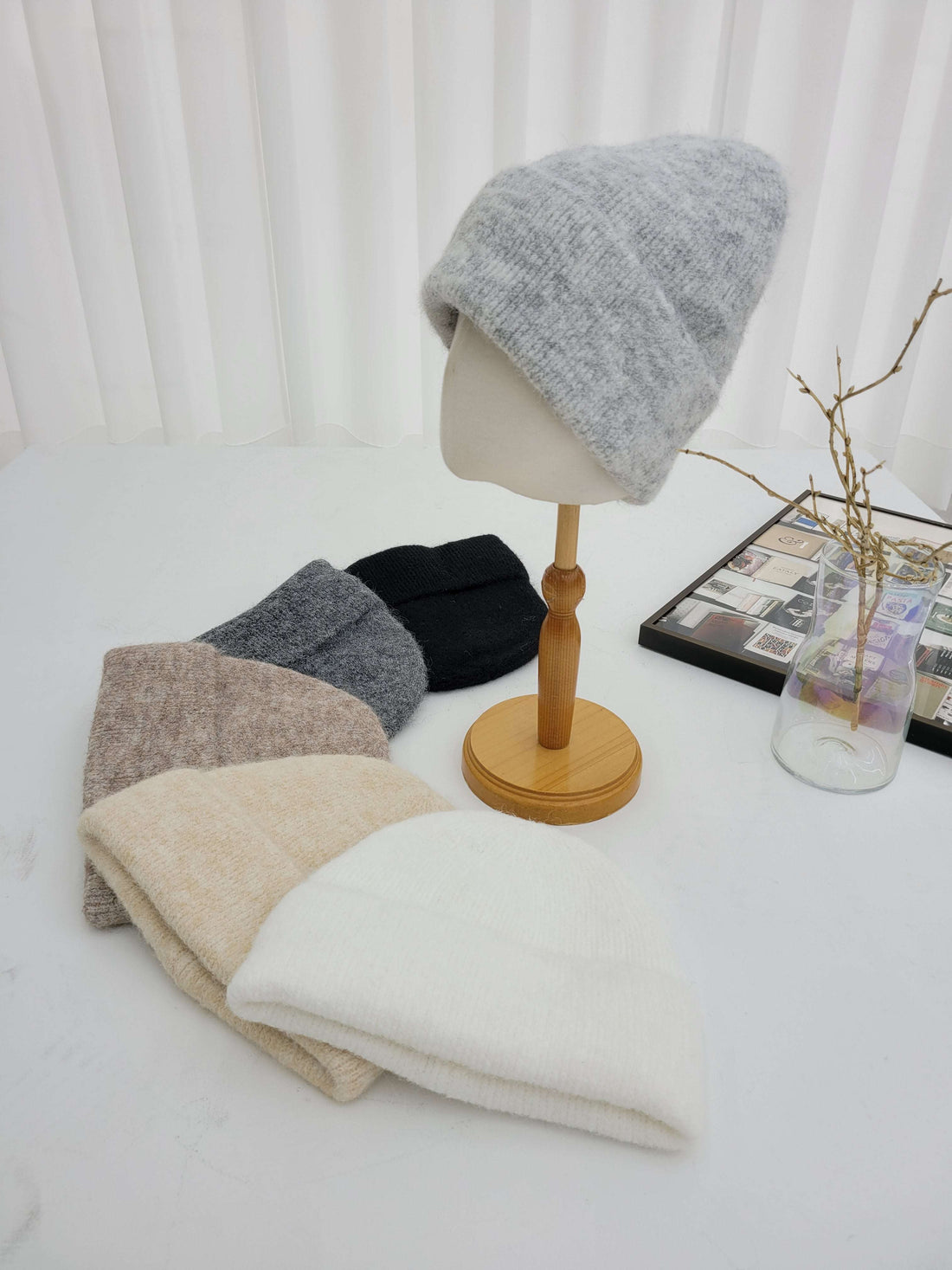 Mannequin head with gray knit cap on a white surface with other caps in the background.