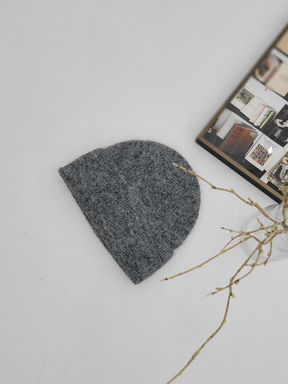 Gray knit beanie on a light gray surface with a branch and magazine in the background