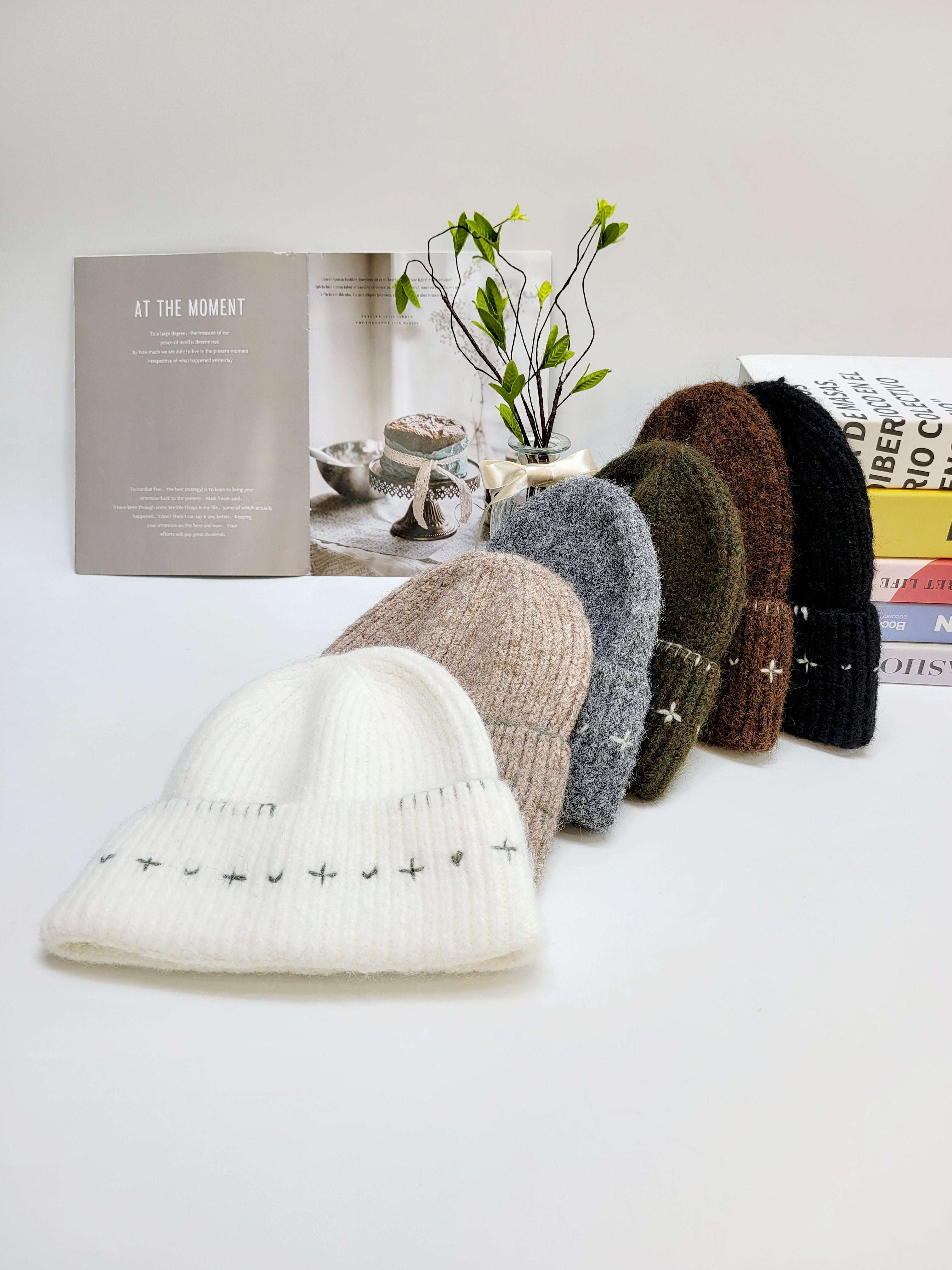 Row of knit hats in various colors on a white surface with a plant and books in the background.