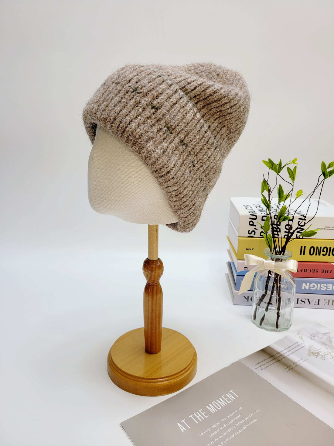 Knitted beanie on a mannequin head with a vase of flowers and books in the background