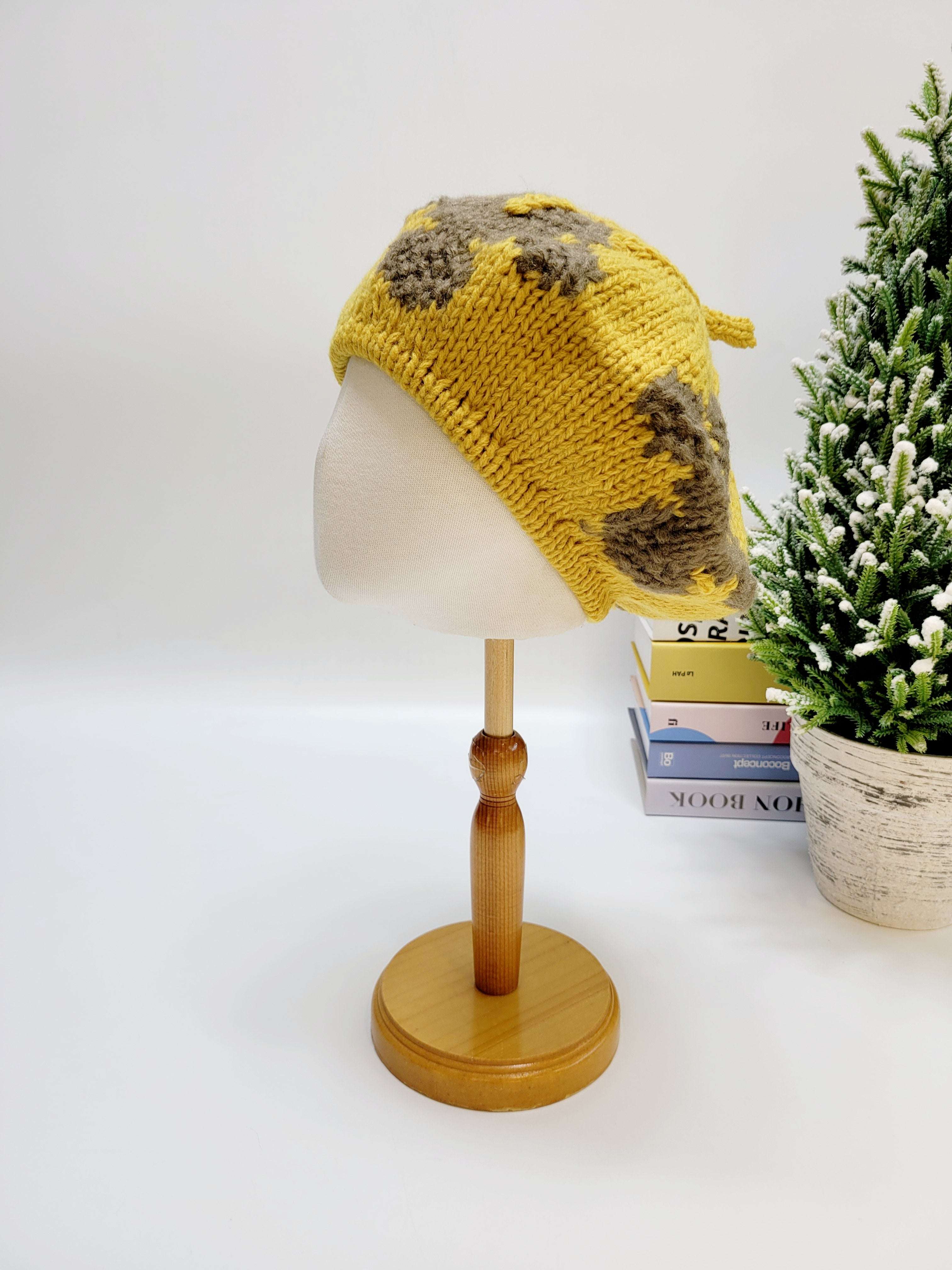 Yellow knitted hat with brown patterns on a mannequin head against a white background.