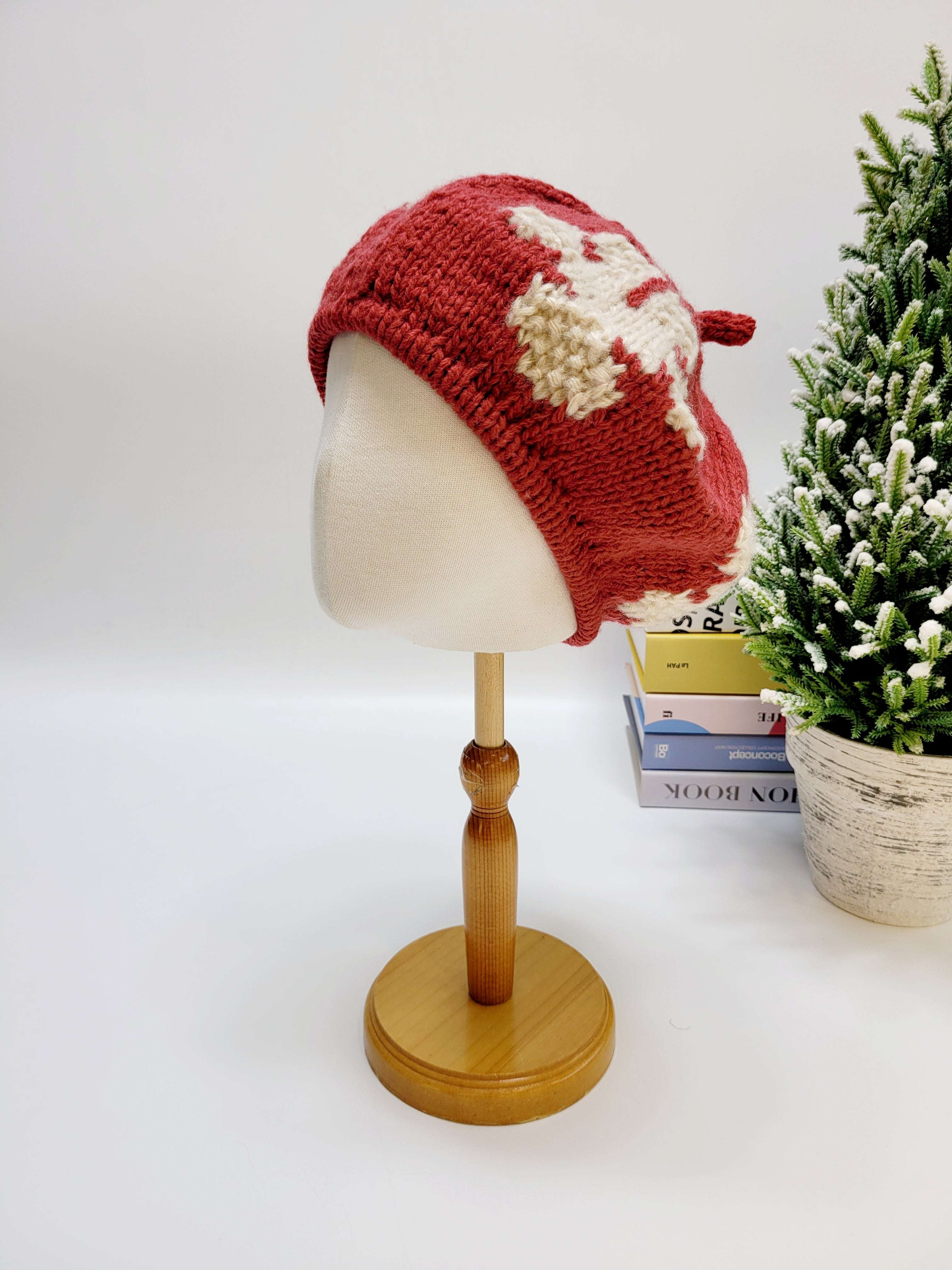 Red knitted hat on a mannequin head with a small Christmas tree in the background