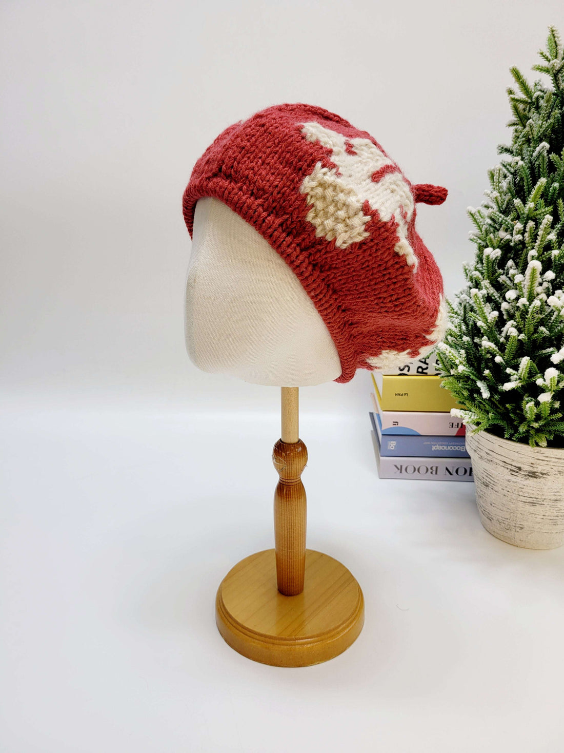 Red knitted hat on a mannequin head with a small Christmas tree in the background