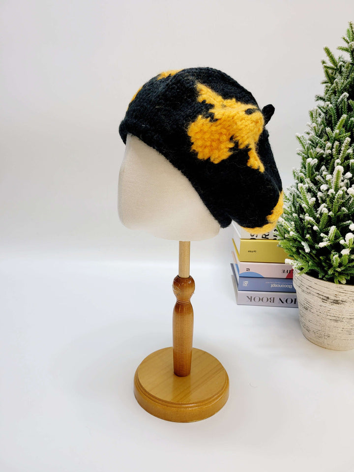 Black and yellow knitted hat on a mannequin head with a Christmas tree in the background