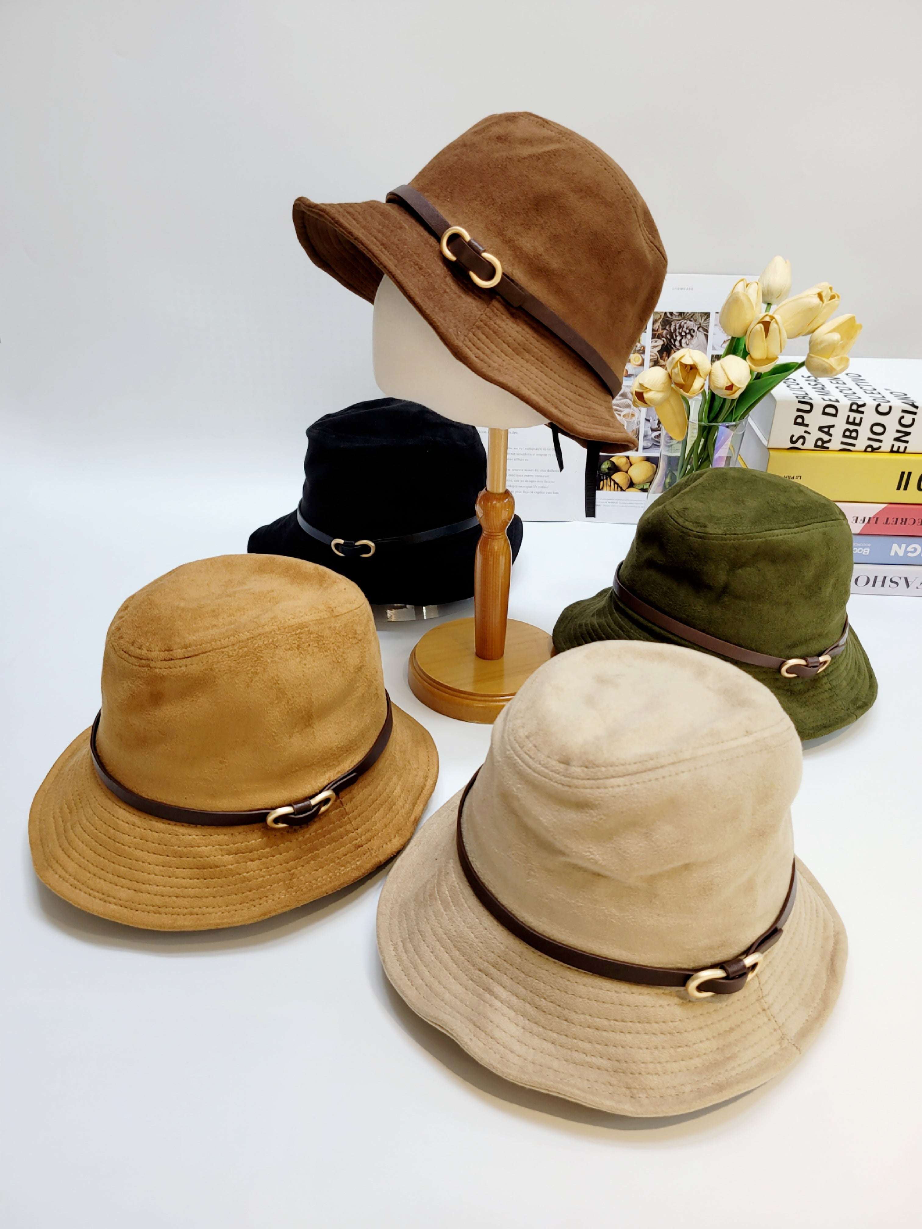 Four different colored bucket hats on a white surface with a vase of flowers in the background.