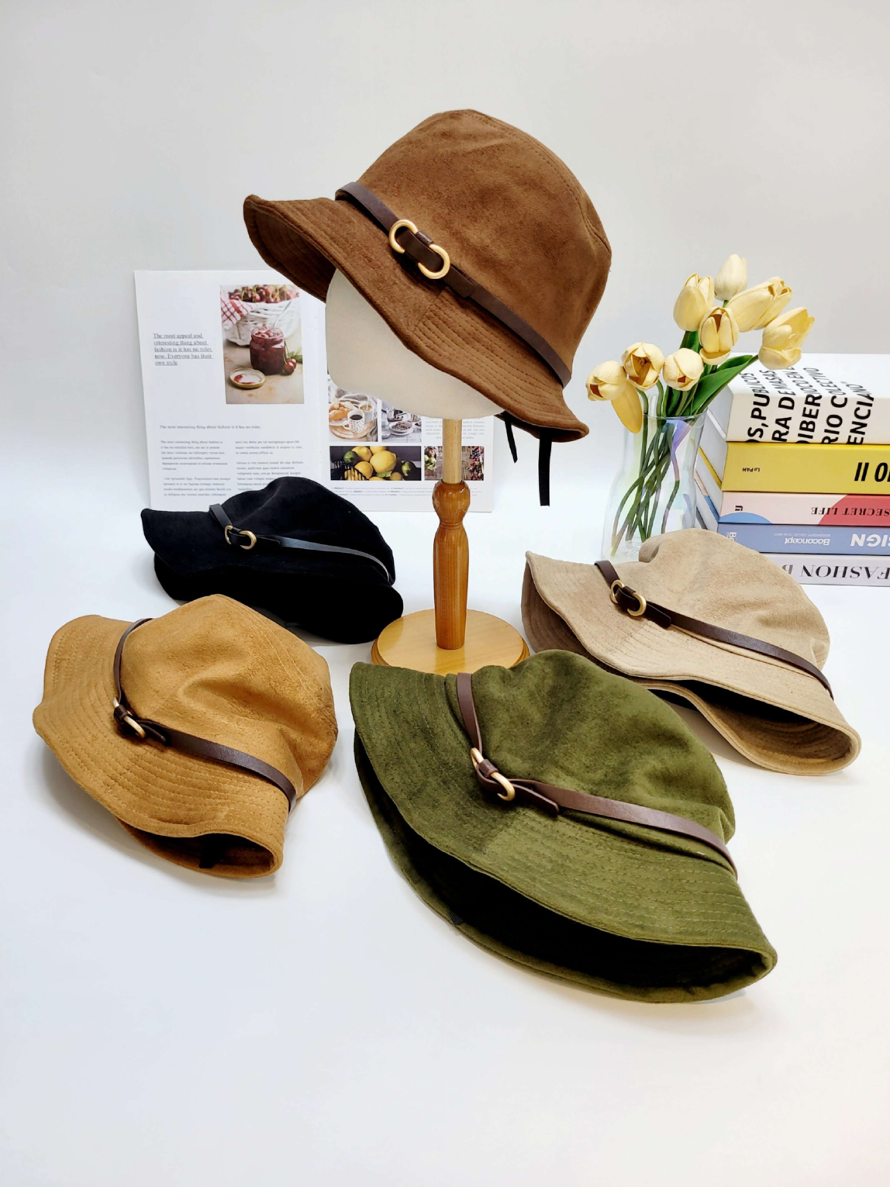 Set of four different colored hats on a white background with a vase of yellow flowers and books.