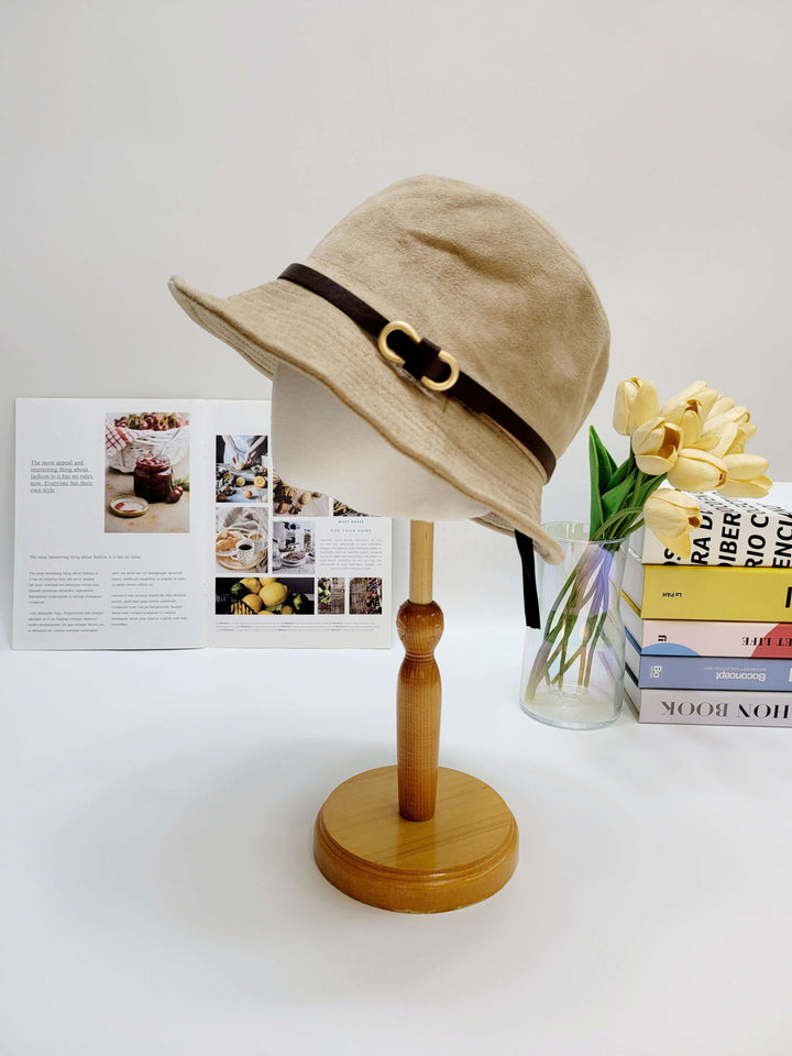 Beige bucket hat with a brown band on a wooden stand against a white background