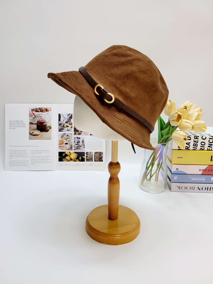Brown bucket hat on a wooden stand with a magazine and books in the background