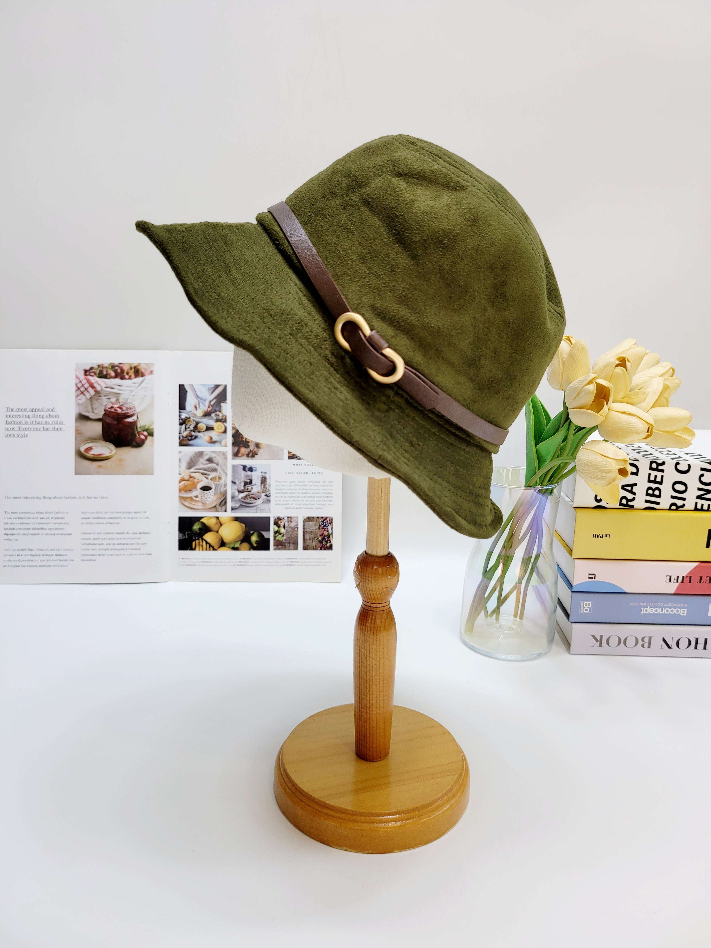 Green bucket hat with a brown strap on a wooden stand against a white background