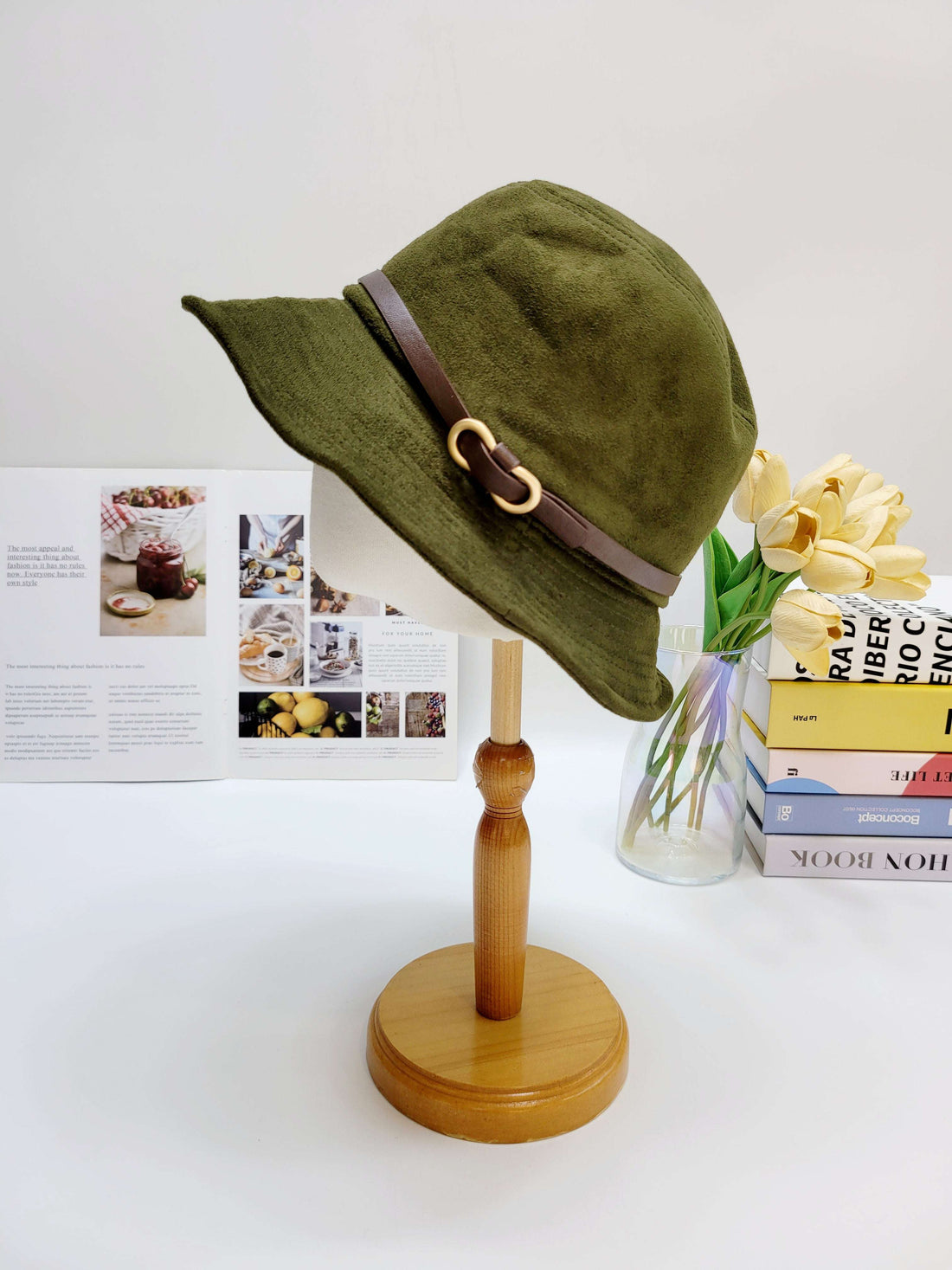 Green bucket hat with a brown strap on a wooden stand against a white background