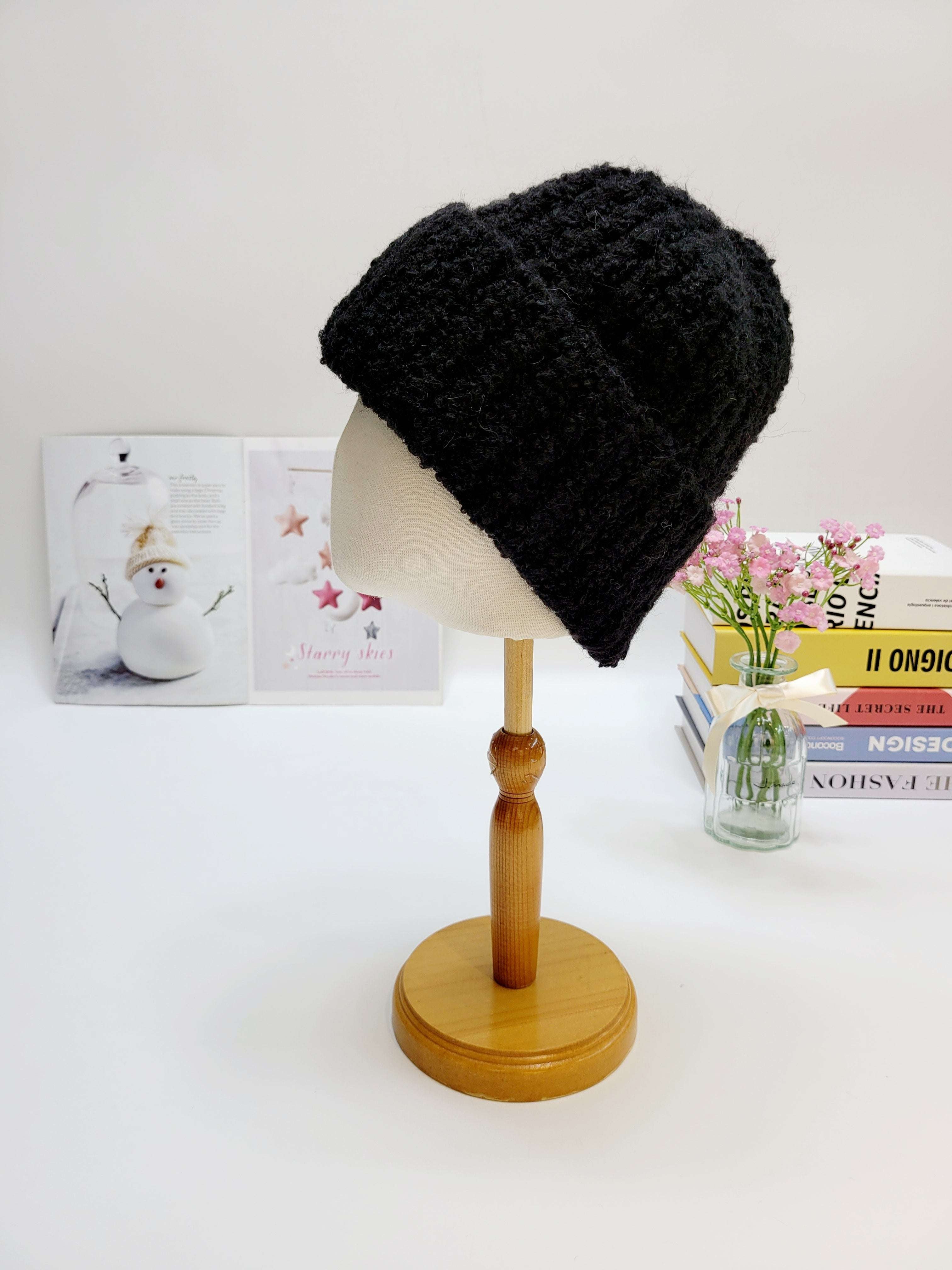 Black knitted beanie on a wooden mannequin head with a light gray background