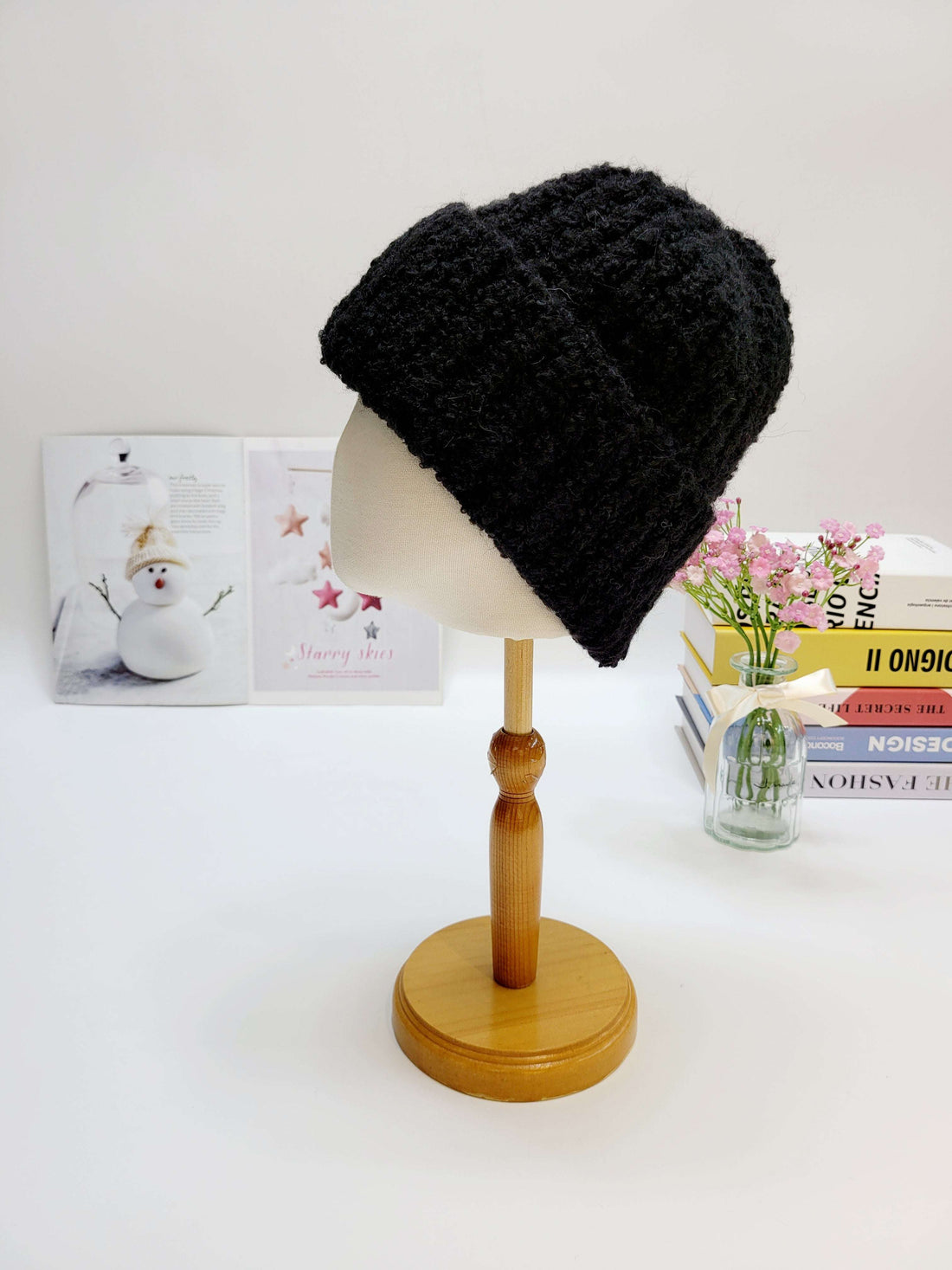 Black knitted beanie on a wooden mannequin head with a light gray background