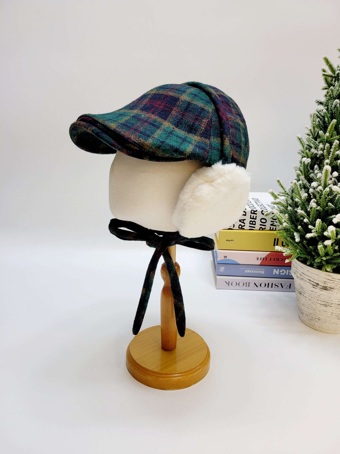 Plaid cap on a mannequin head with a white background and books in the background