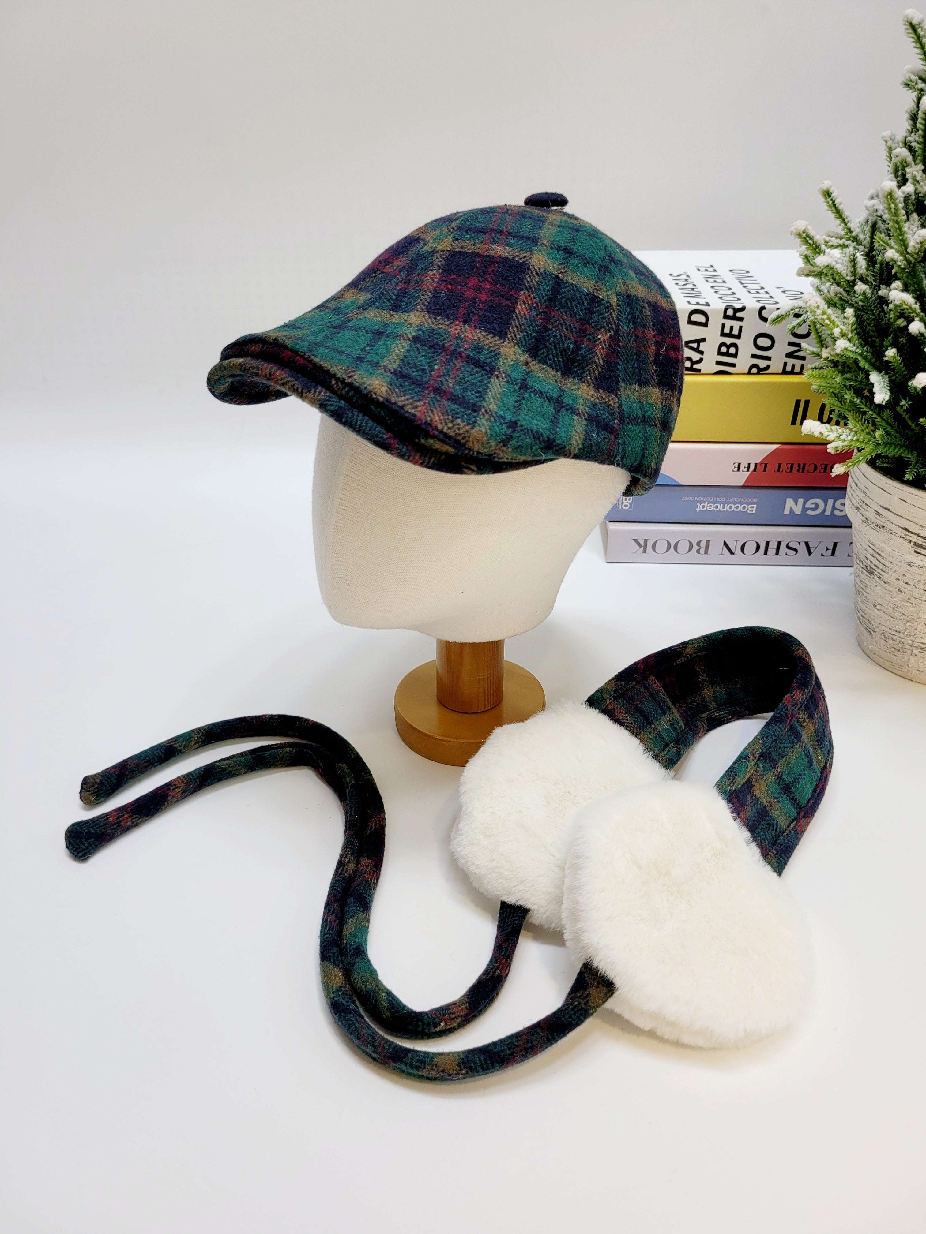 Plaid cap and ear muffs on a mannequin head with books and a plant in the background.