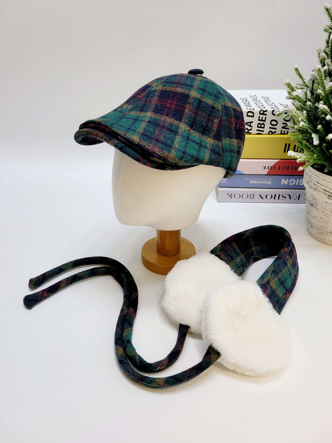 Plaid cap and ear muffs on a mannequin head with books and a plant in the background.