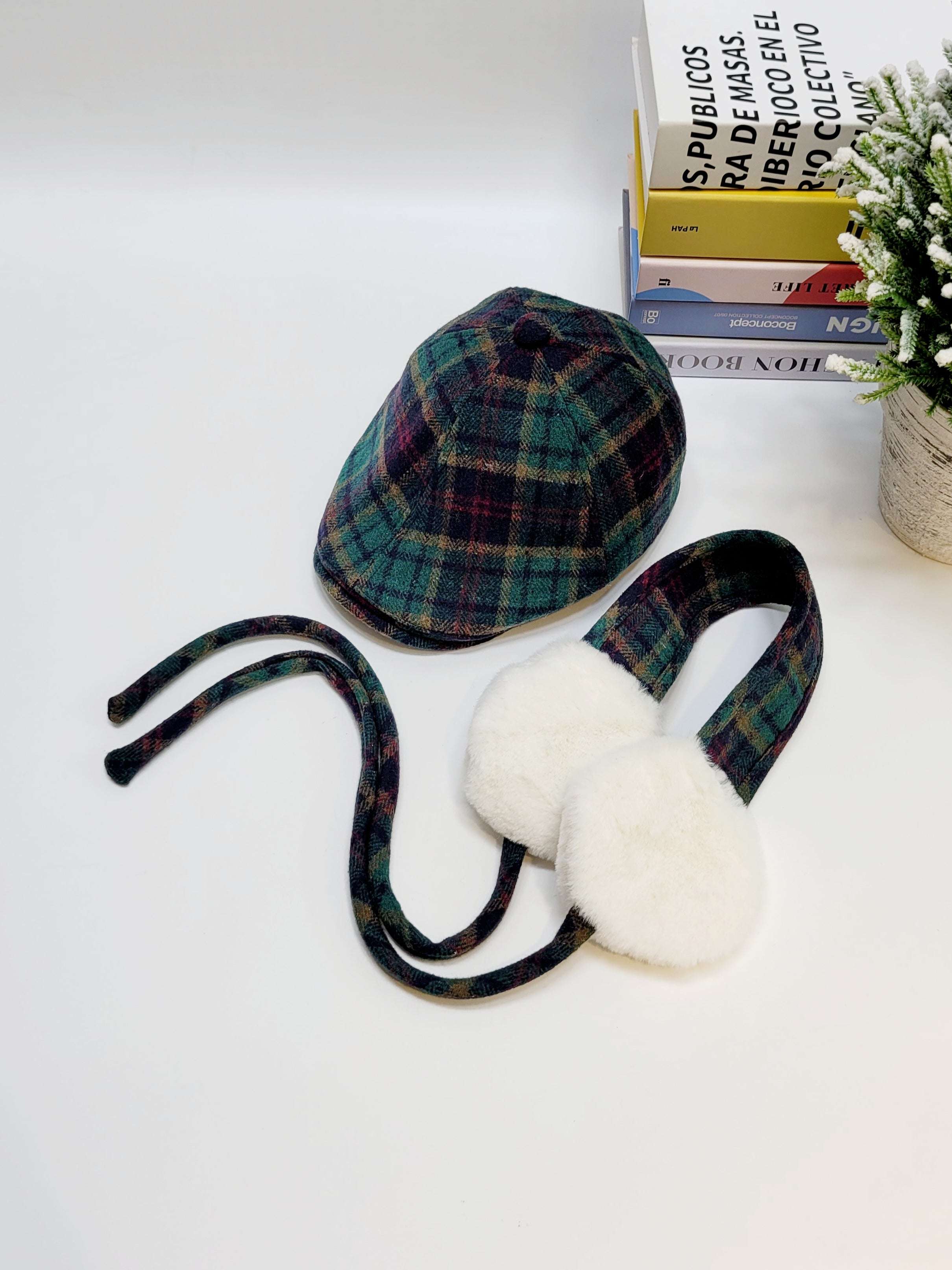 Plaid hat and ear muffs on a white surface with books and a plant in the background