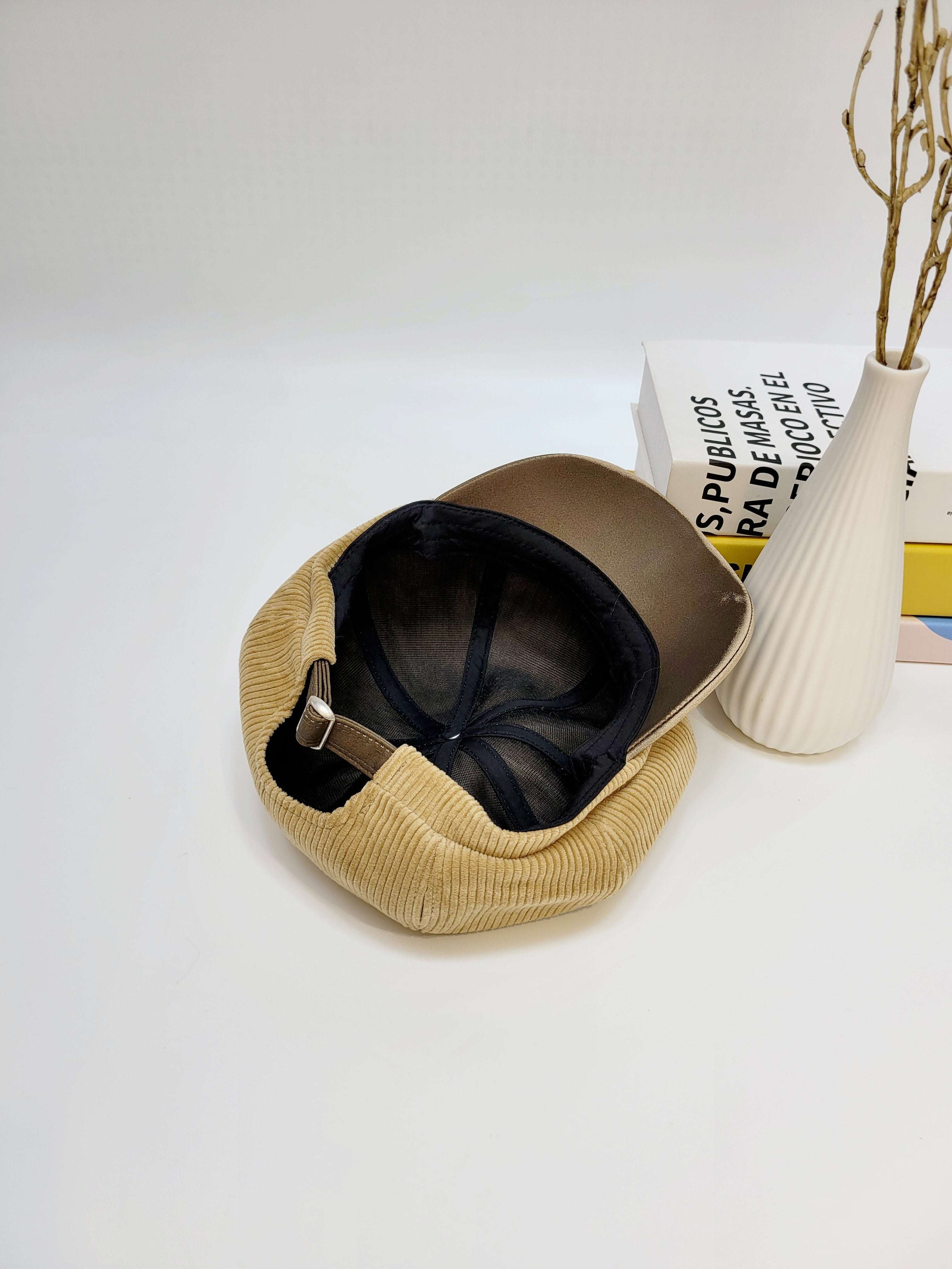 Beige cap with black interior on a white surface with a vase and books in the background