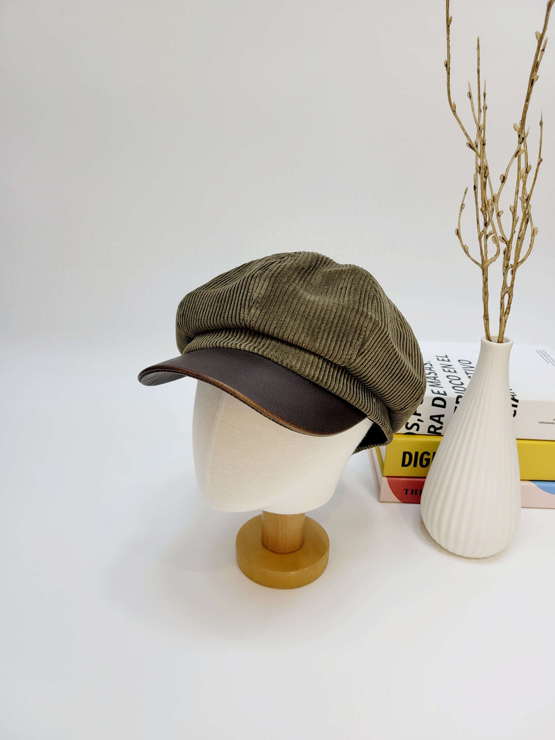 Green corduroy cap with brown leather visor on a mannequin head against a white background.