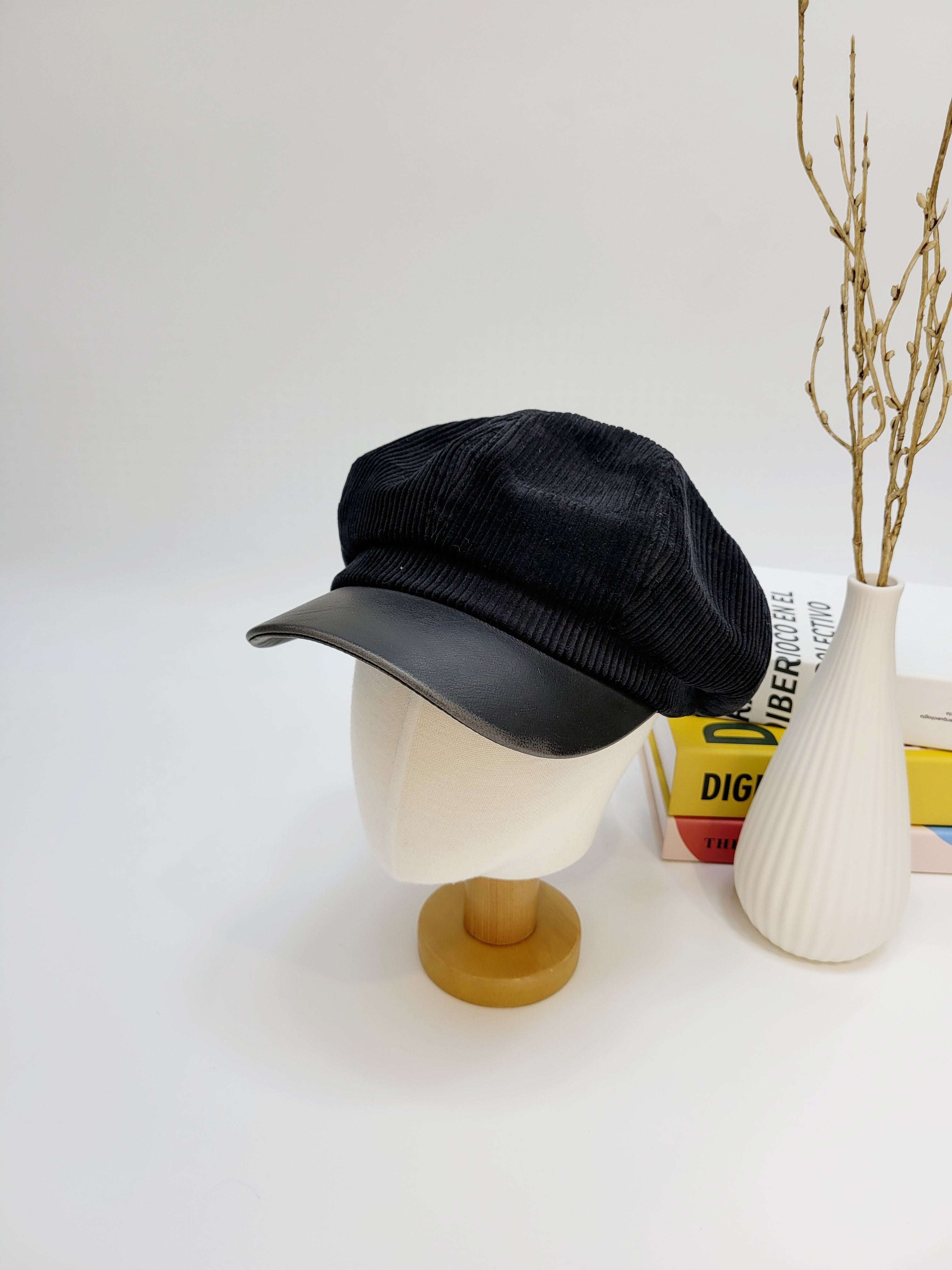 Black cap on a mannequin head with a white vase and books in the background