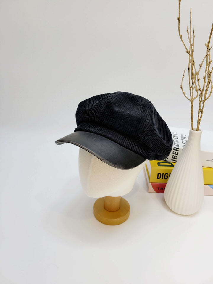 Black cap on a mannequin head with a white vase and books in the background