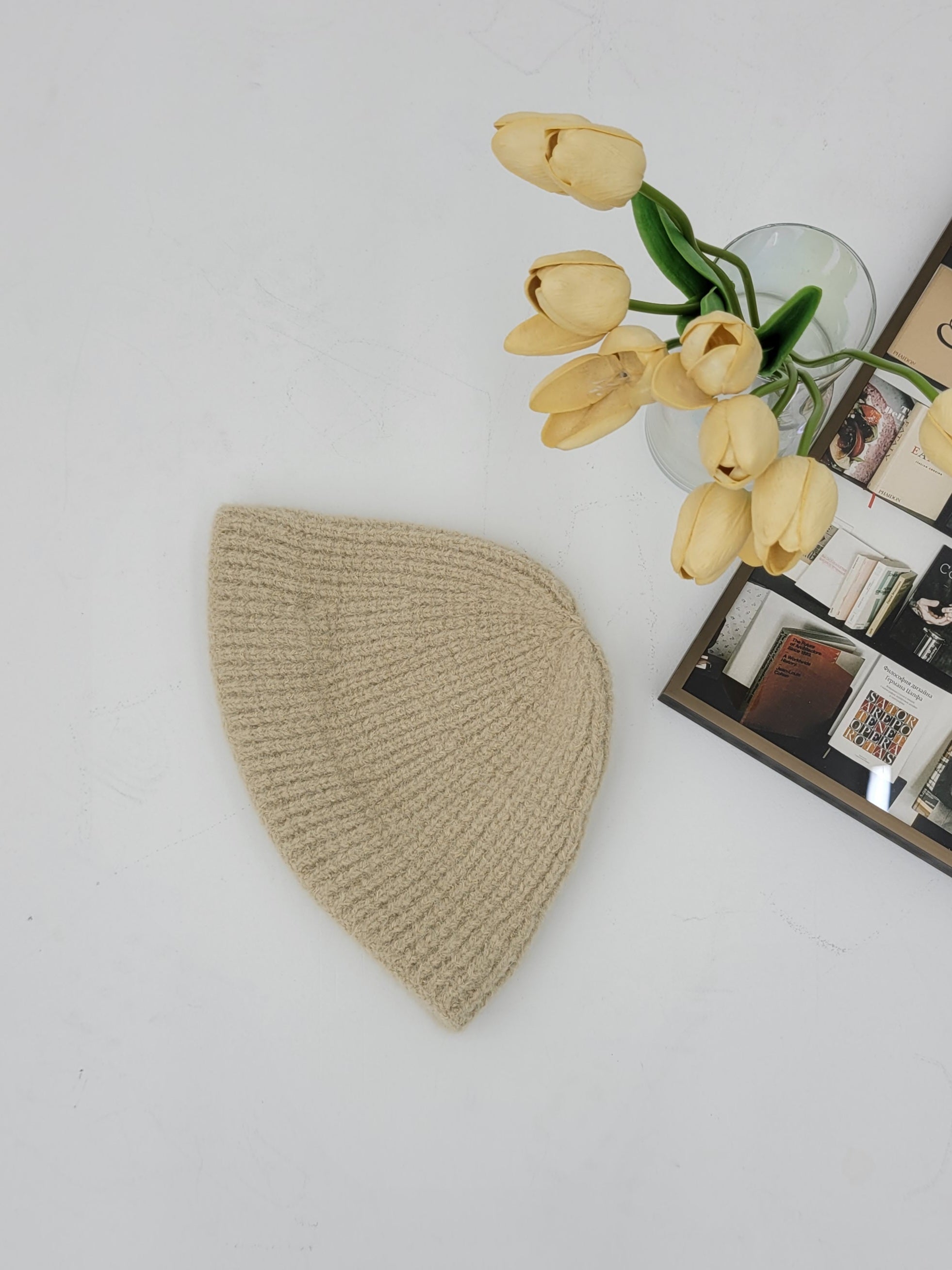 Beige knitted heart-shaped object on a white surface with yellow tulips in the background.