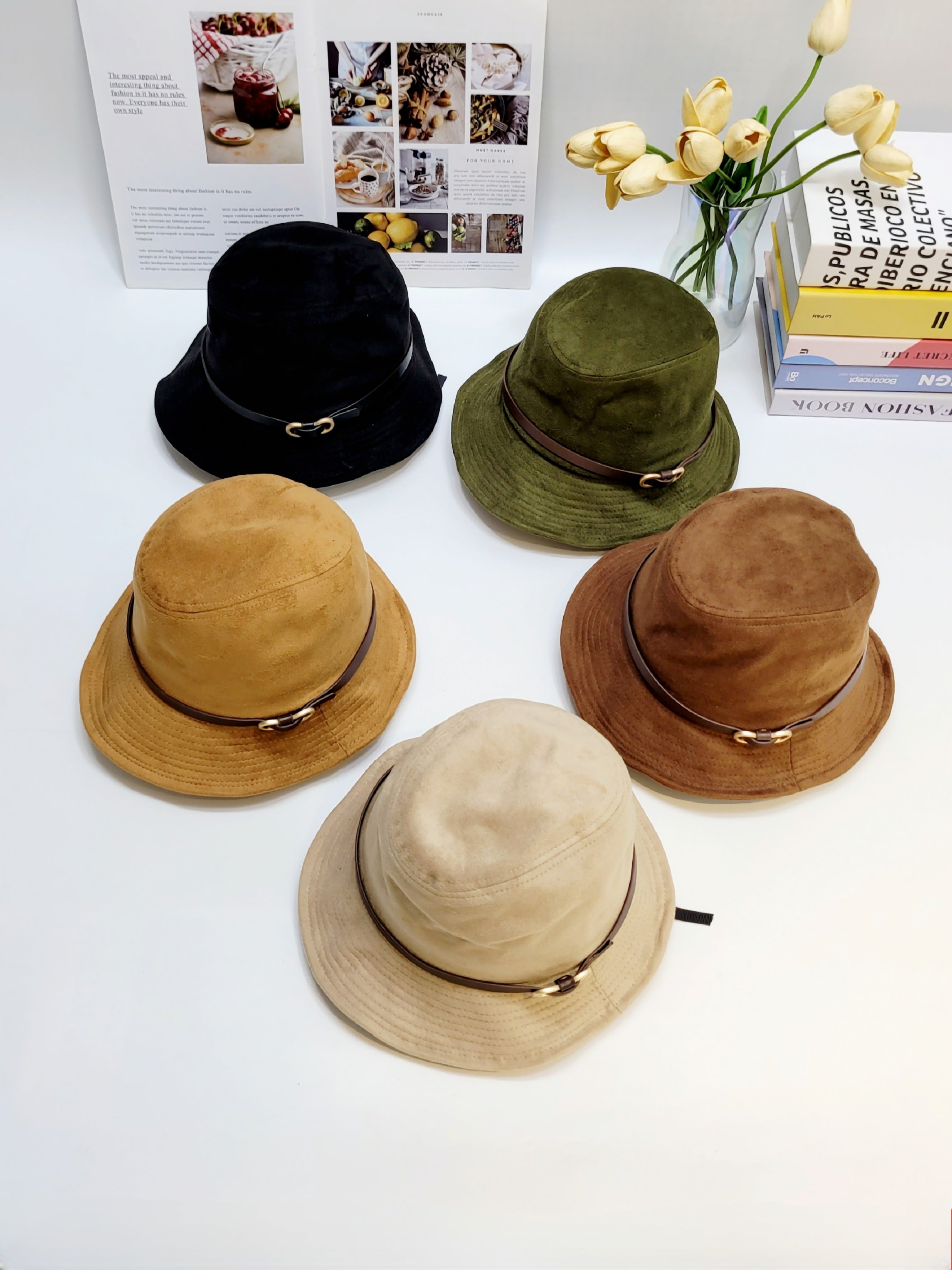 Five different colored hats on a white surface with a magazine and flowers in the background.