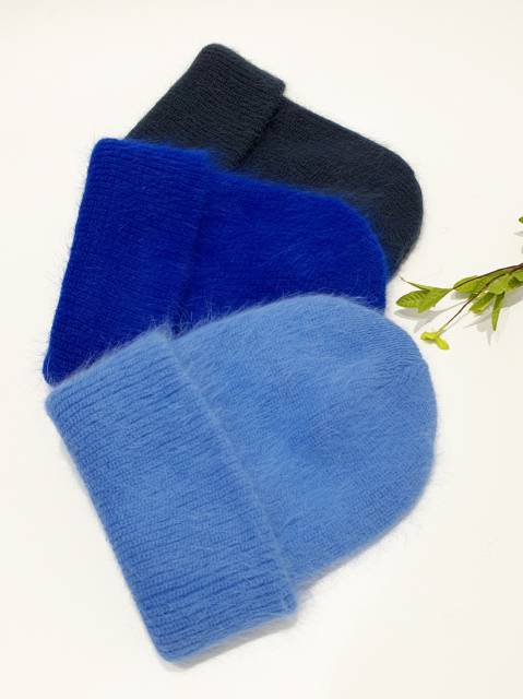 Three knit hats in blue, black, and gray on a white background with green leaves.