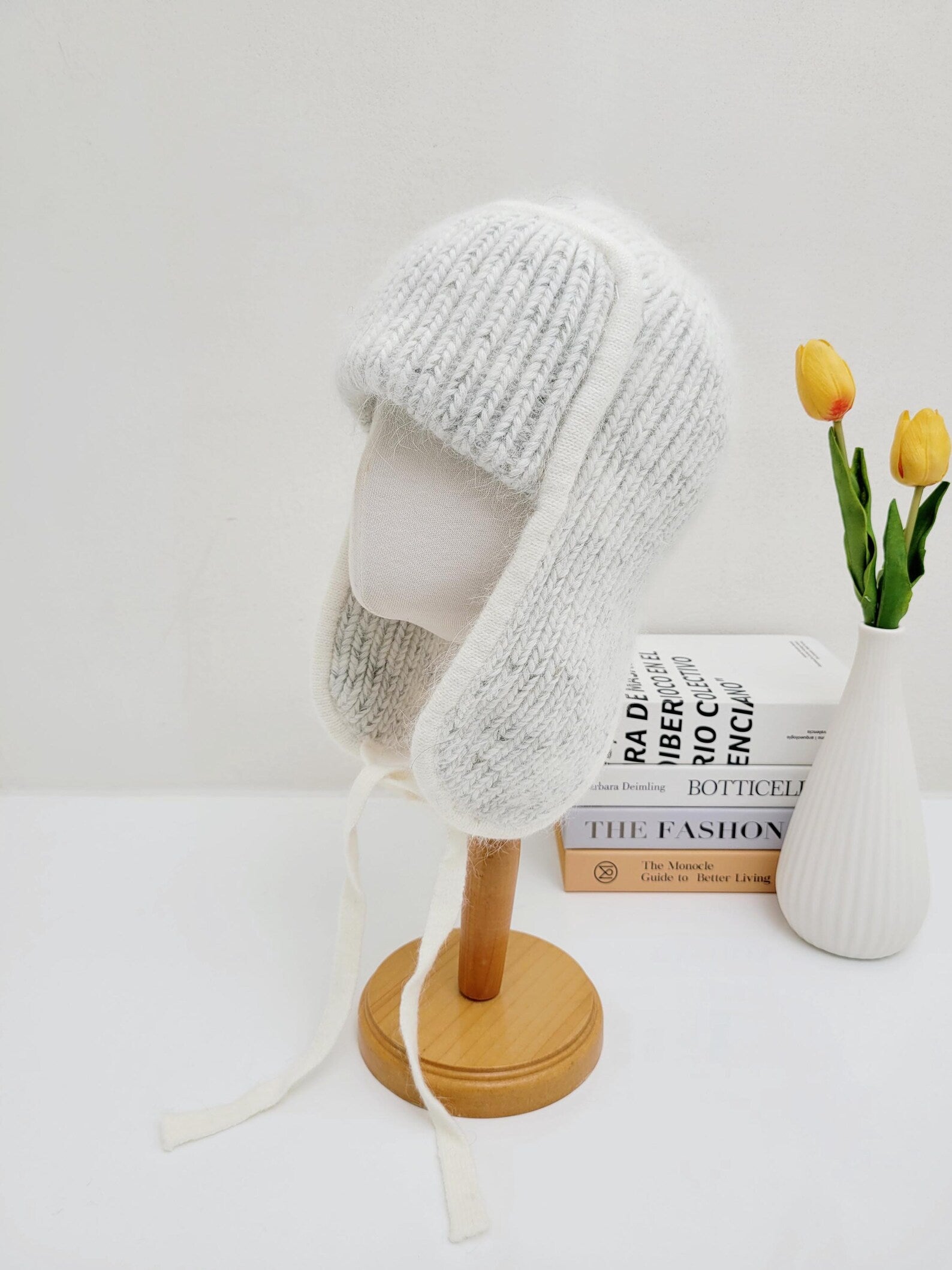 west mountain angora trapper hat: soft grey knit with ear flaps and tie strings, displayed on a wooden stand.