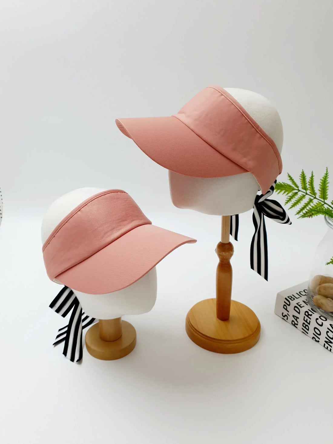 Two pink lic visor hats with black and white striped ribbon ties, displayed on mannequin heads.