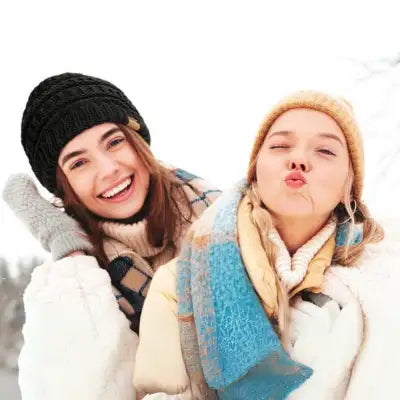 Two smiling women in winter hats and scarves pose outdoors.