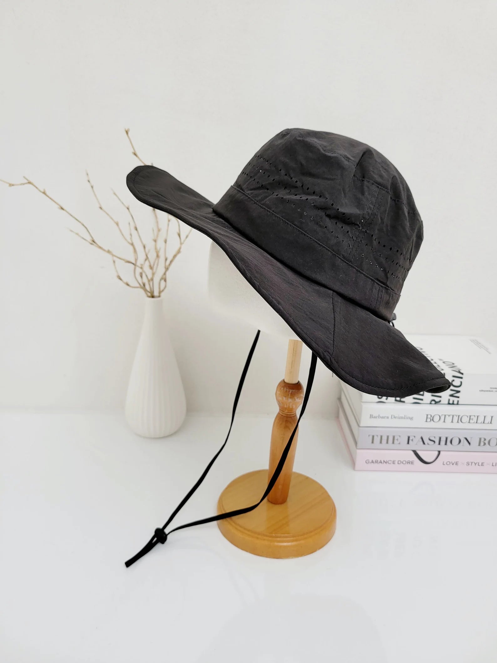 long journey black bucket hat with chin strap on a wooden stand. Lightweight material, wide brim for sun protection, ideal travel hat for outdoor adventures and hiking.