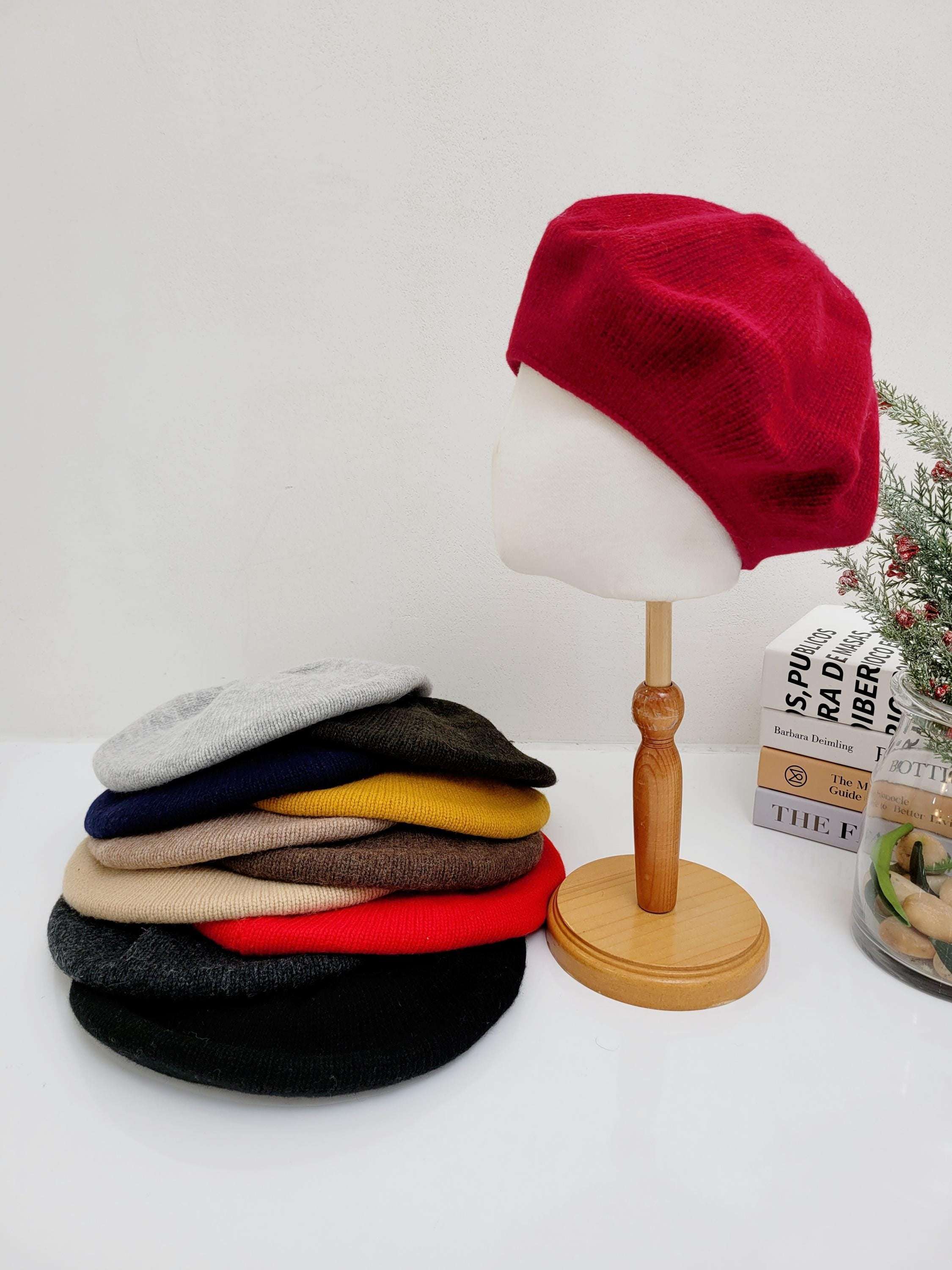 Stack of paris wool beret hats in various colors (red, grey, black, beige, mustard, navy, olive), with a red beret displayed on a mannequin head.