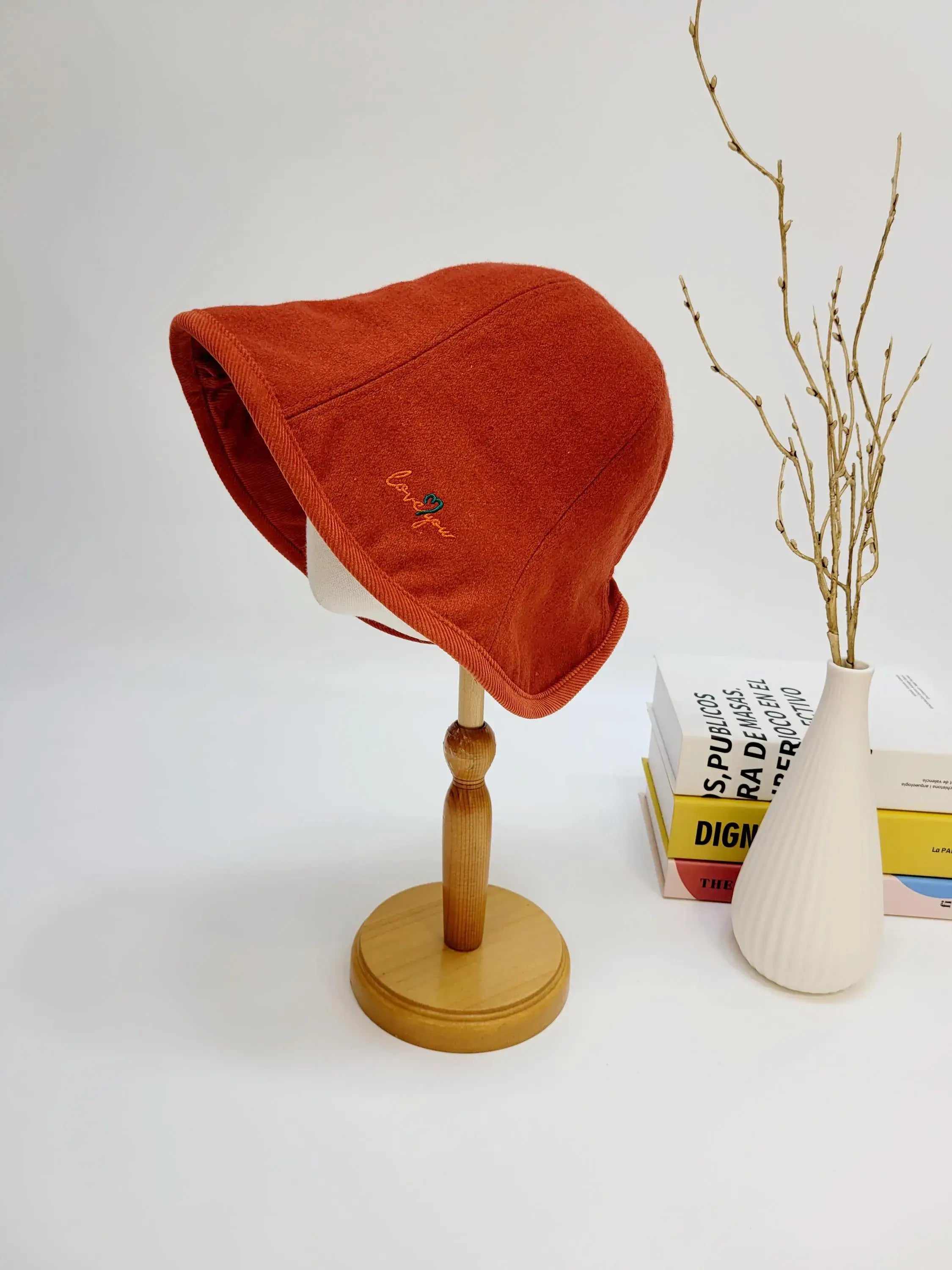 Rust-colored wool bucket hat with "love you" embroidery detail, displayed on a wooden stand.