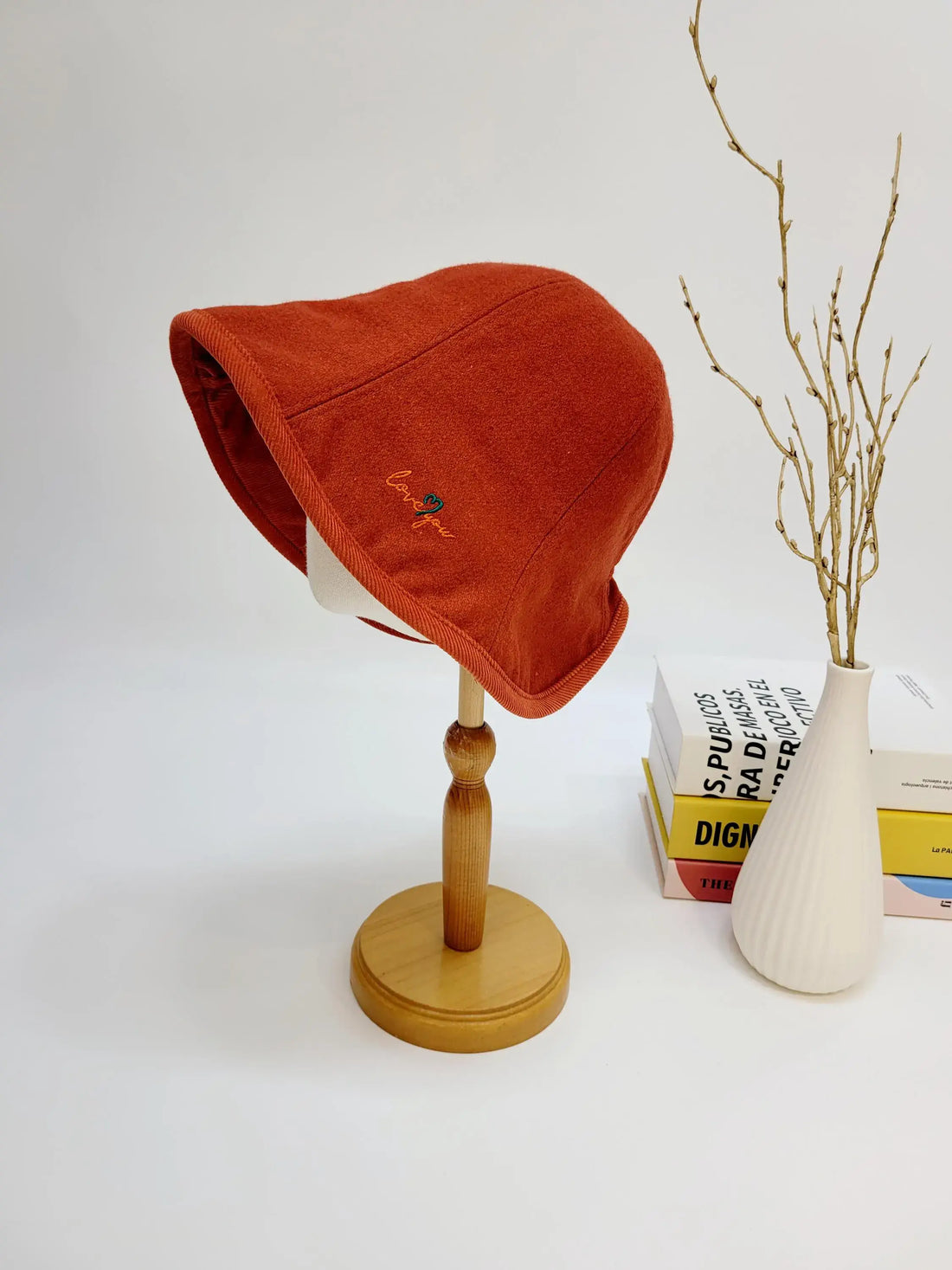Rust-colored wool bucket hat with "love you" embroidery detail, displayed on a wooden stand.