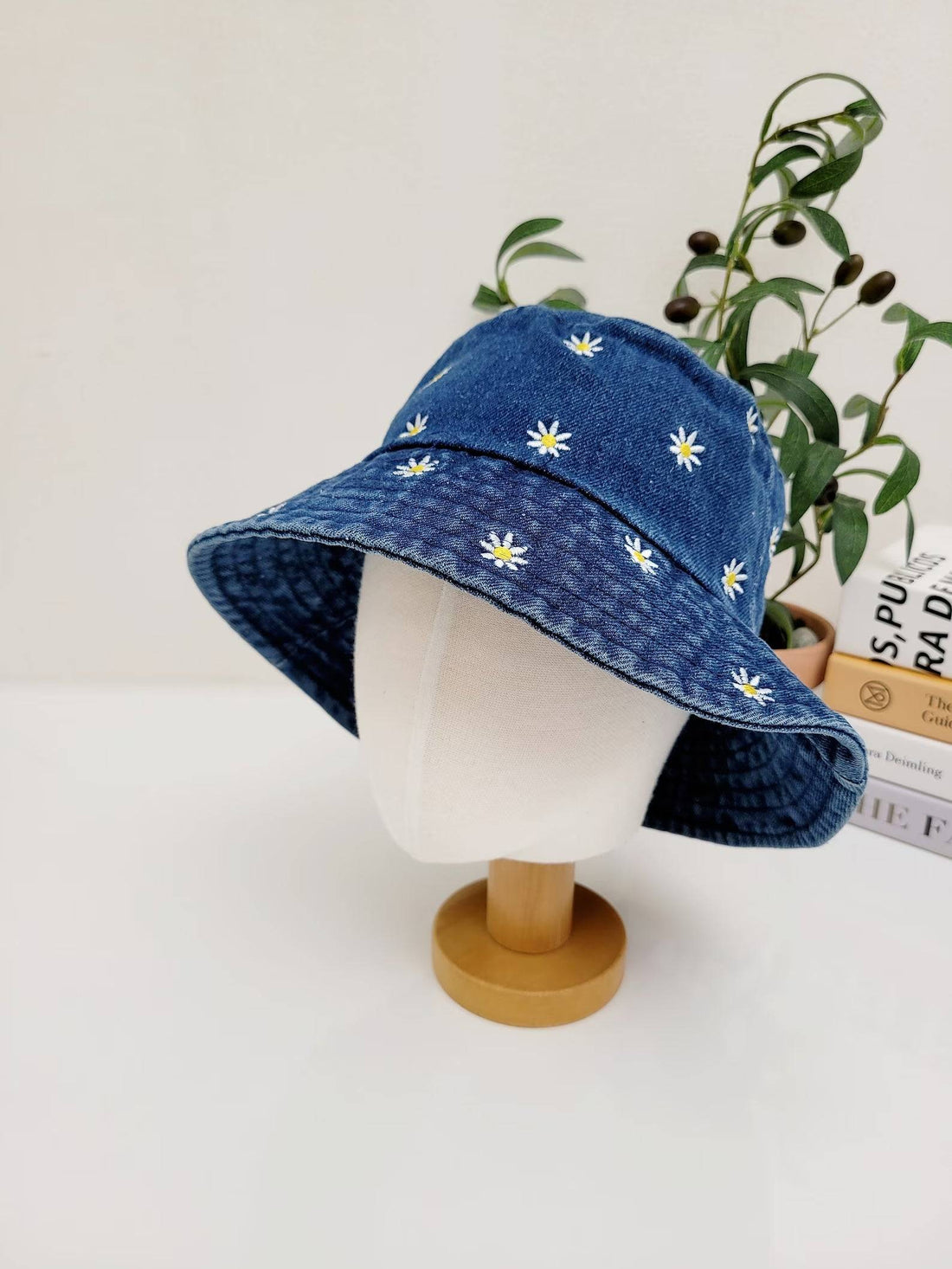 daisy denim bucket hat: Blue denim hat with embroidered white daisies, displayed on a mannequin head. Stylish and casual sun protection.