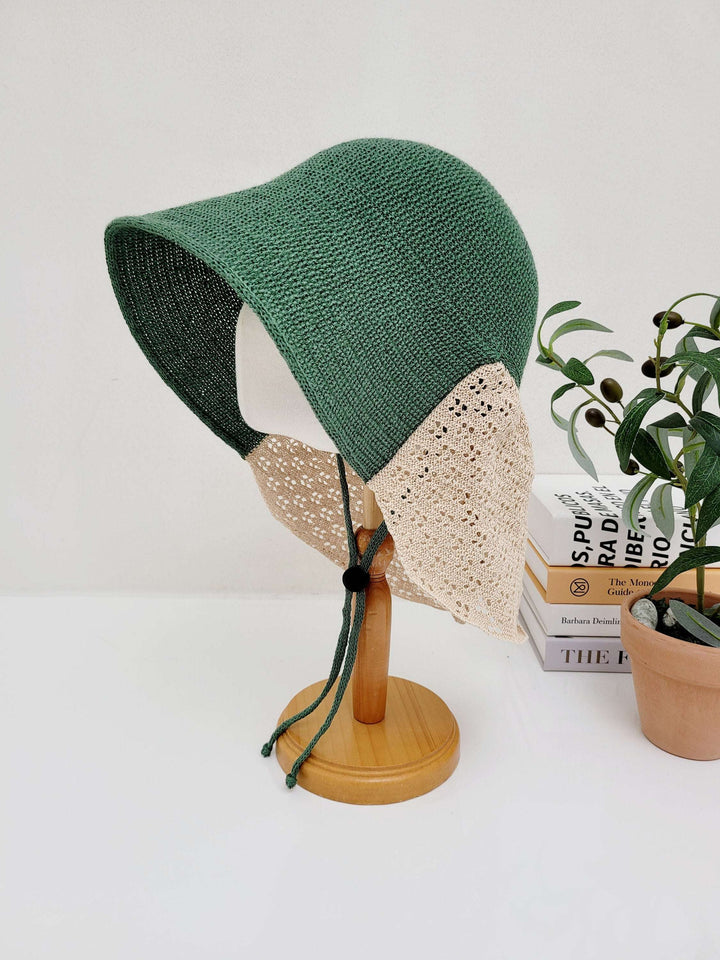 Green sun hat with beige lace trim and tie strings, displayed on a wooden stand. The celine hat offers sun protection with a touch of vintage charm.