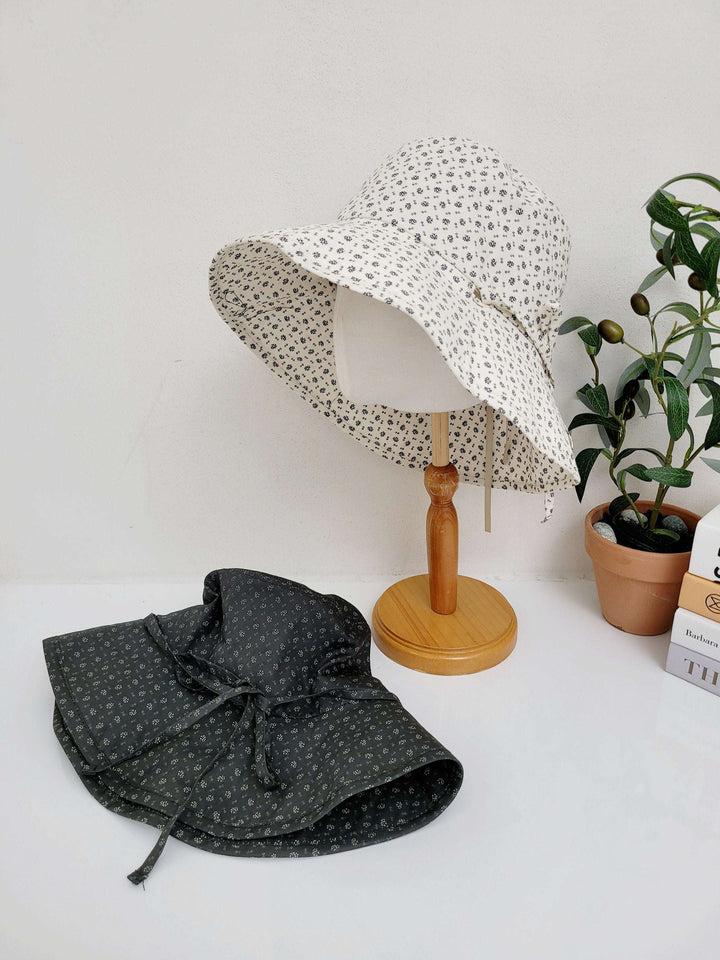 Two light weight wide brim hats: one cream floral hat on a mannequin, and a dark gray floral hat folded on a white surface