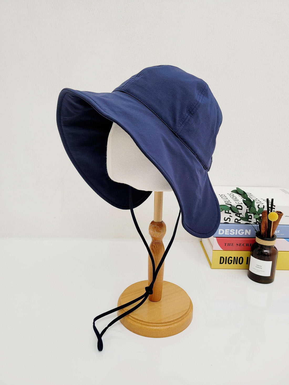 Navy blue summer large brim hat on a wooden display stand, featuring a wide brim and adjustable black chin strap.