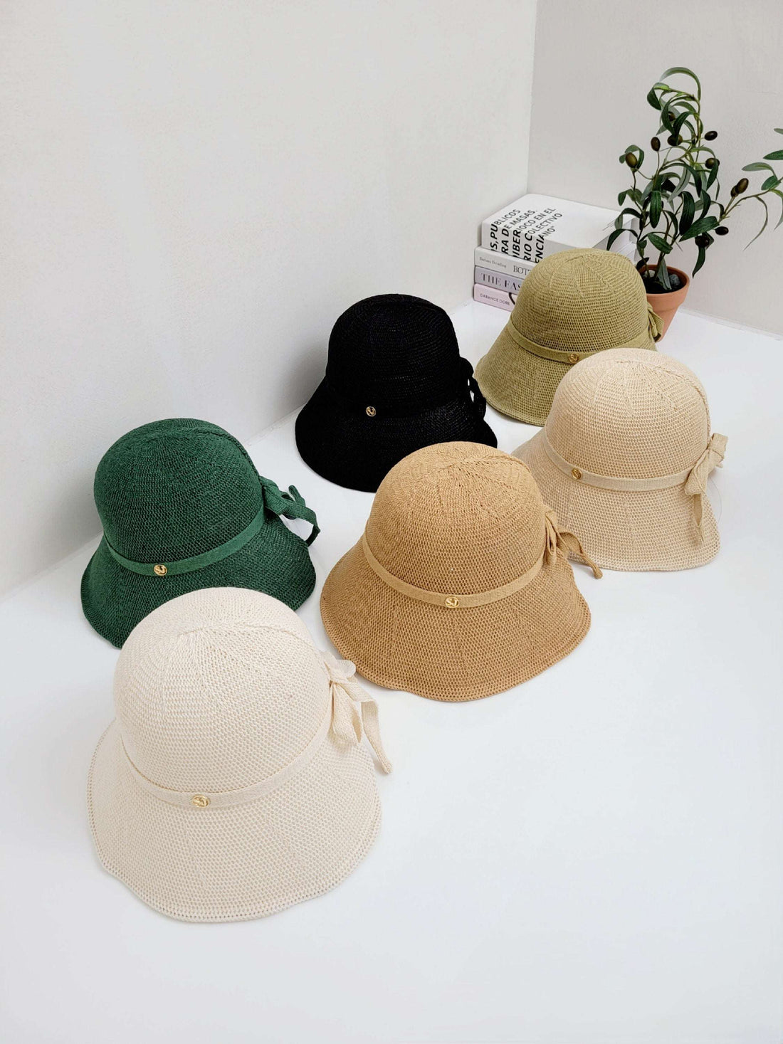 Six knitted sun hats in cream, tan, green, olive, black, and beige, each with a ribbon detail, arranged on a white surface